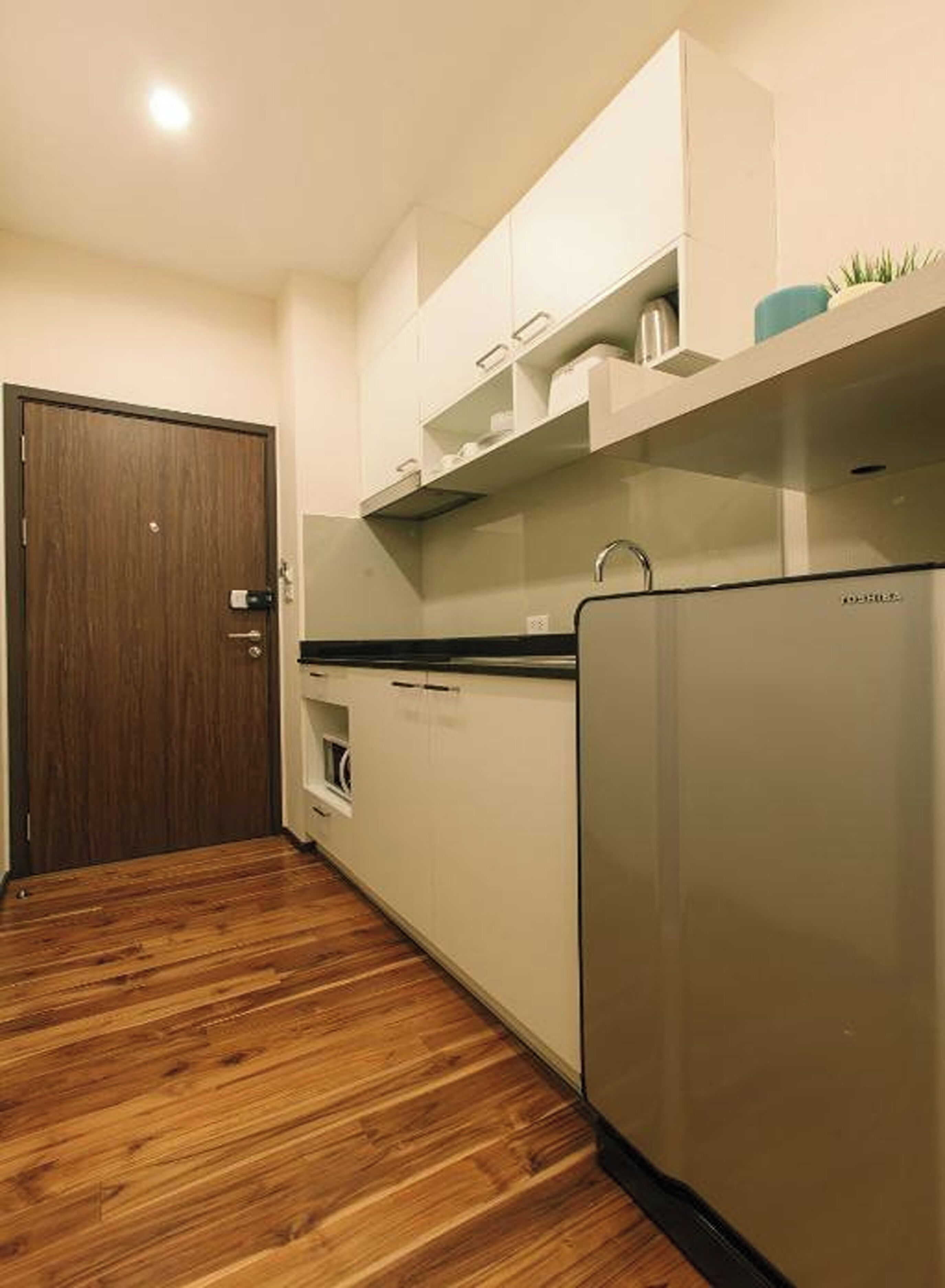 A compact kitchen with white cabinets, a stainless steel refrigerator, and a wooden floor.