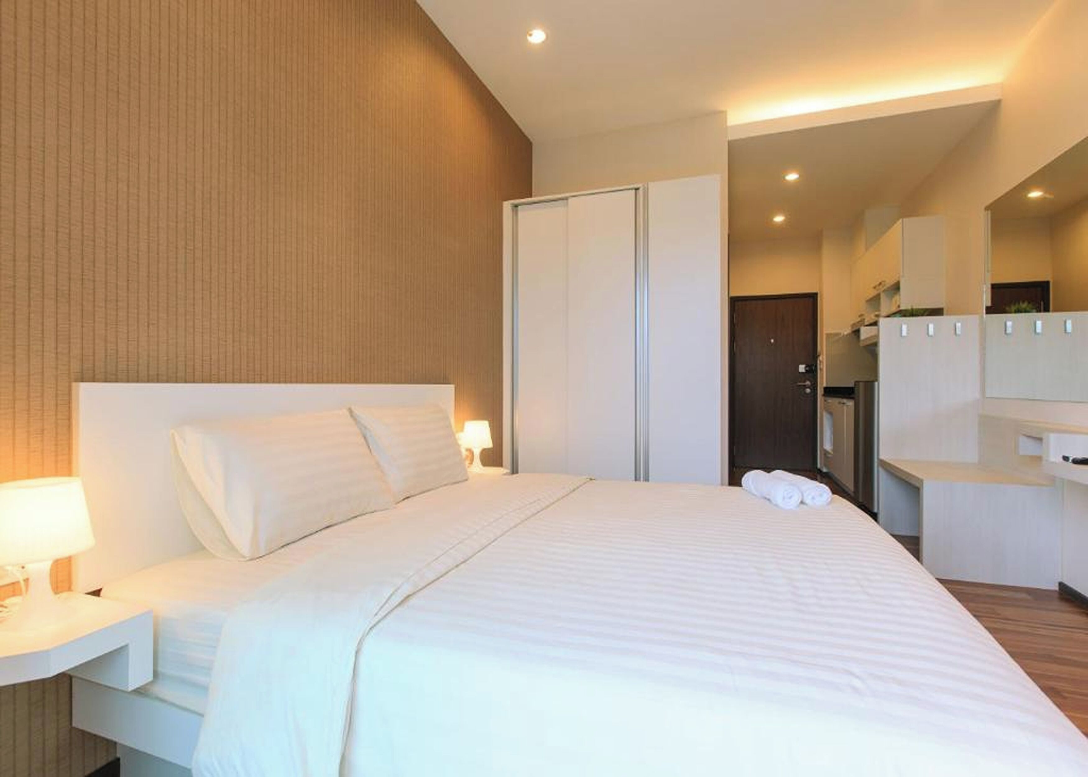 A modern hotel room with a large bed, a nightstand, a desk, and a wardrobe.