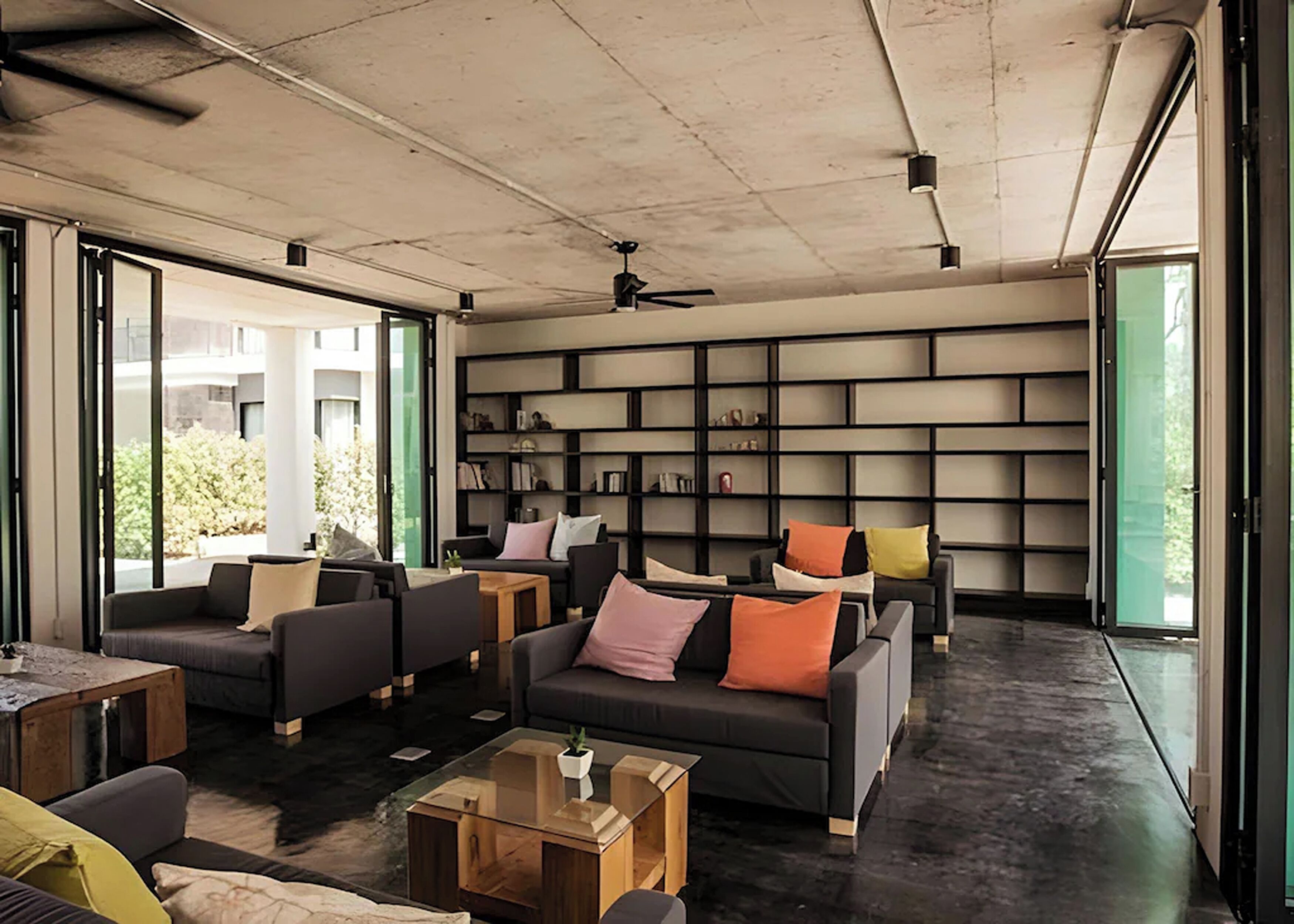 Ein modernes Wohnzimmer mit einer großen Bücherwand, bequemen Sitzmöglichkeiten und großen Fenstern.