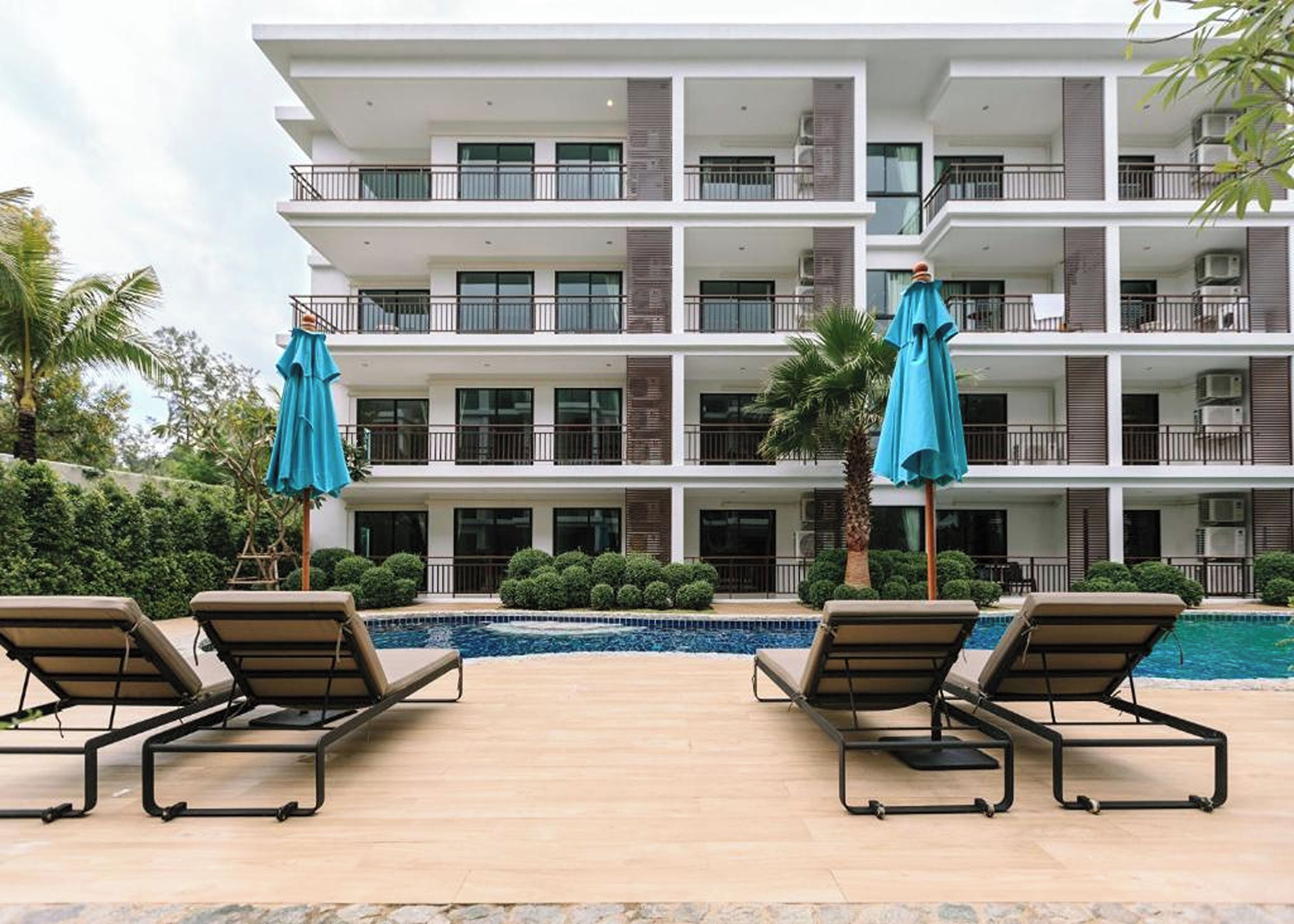 Un hotel de varios pisos con una zona de piscina, que incluye sillas de descanso y sombrillas.