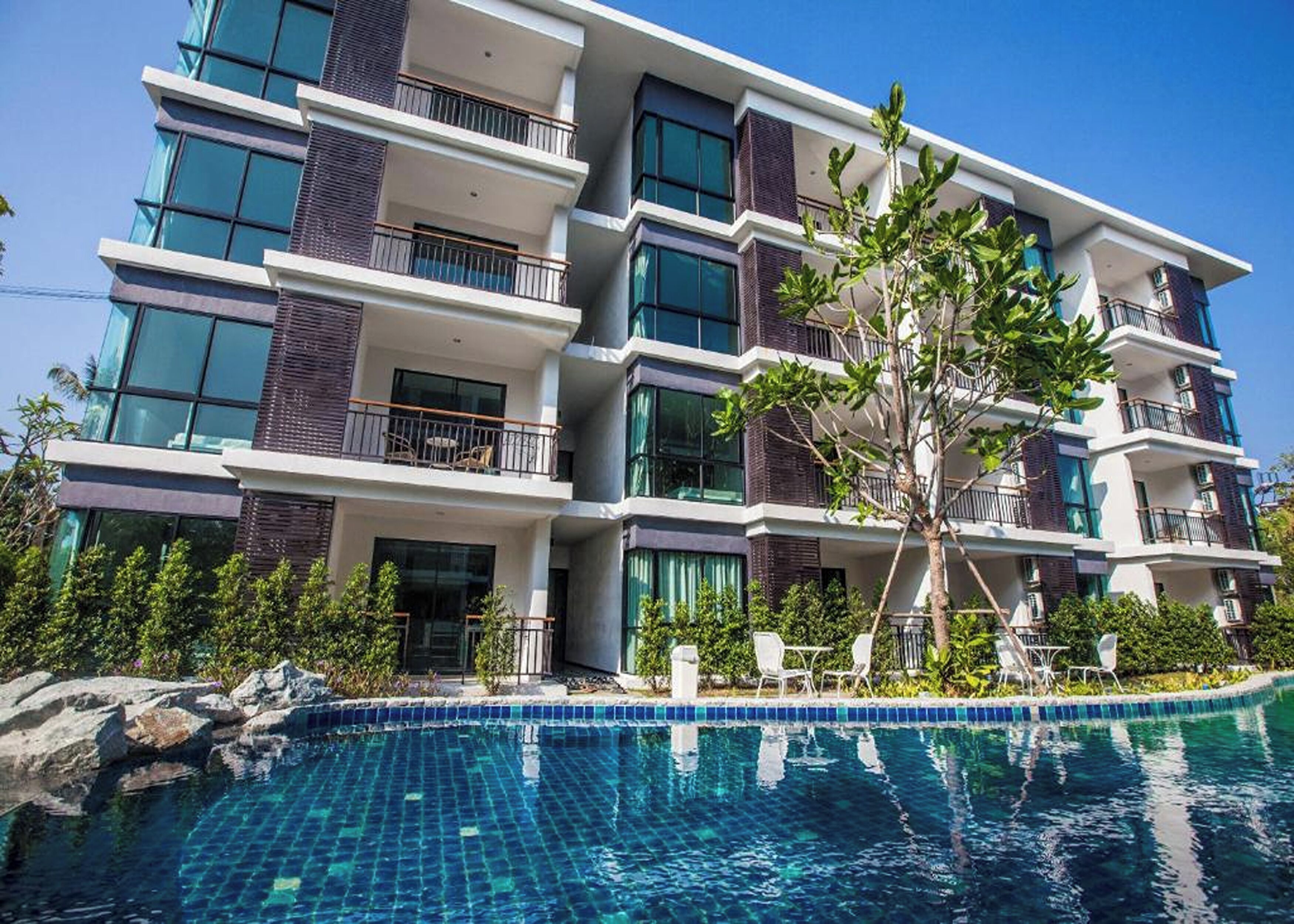 A multi-story hotel with balconies, a swimming pool, and lush greenery.
