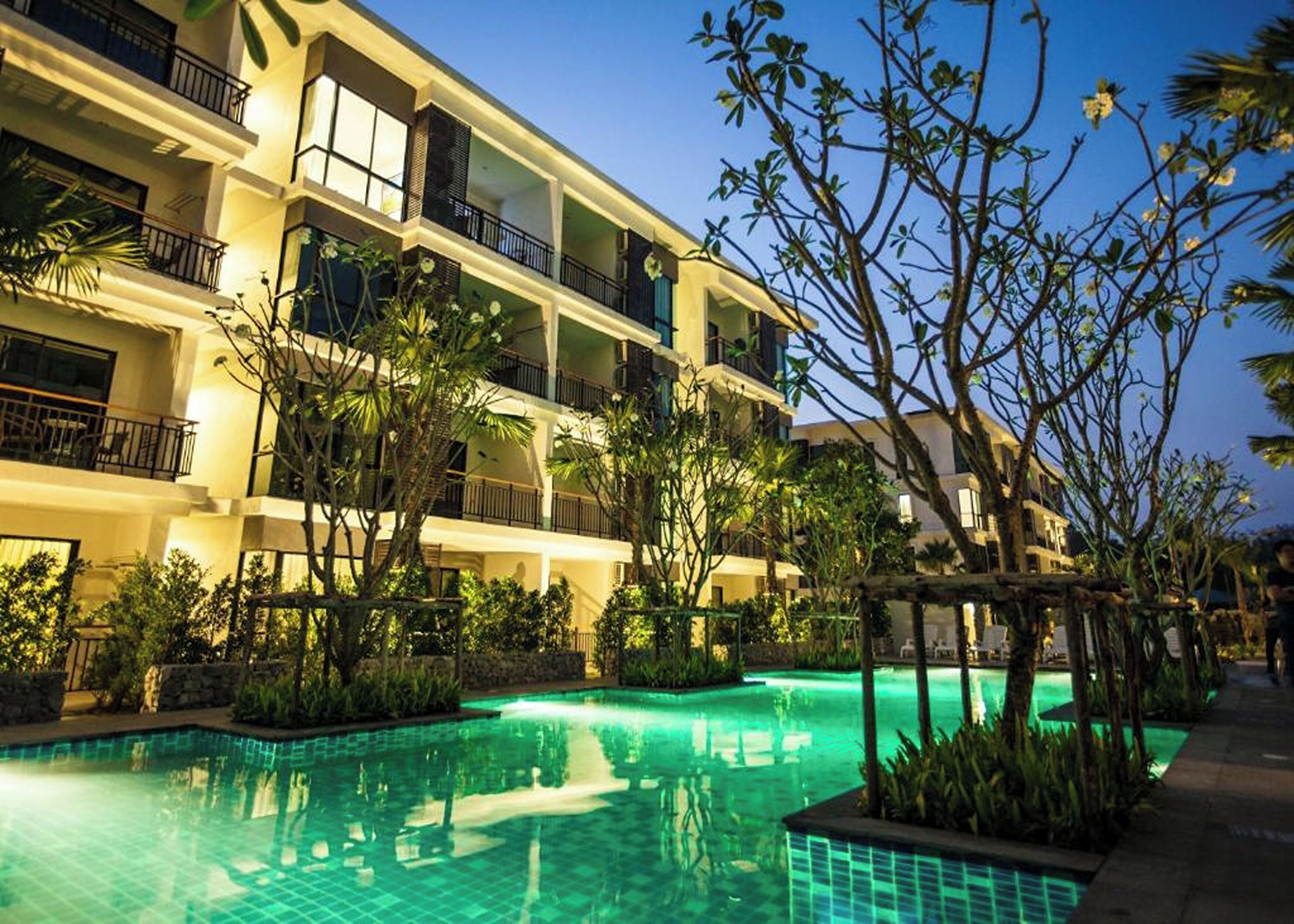 A multi-story hotel with balconies, a swimming pool, and tropical landscaping.