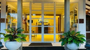 Entrada de un hotel con puerta de vidrio, un cartel que dice "Salsa Hotel & Resort" y dos plantas en macetas a cada lado.