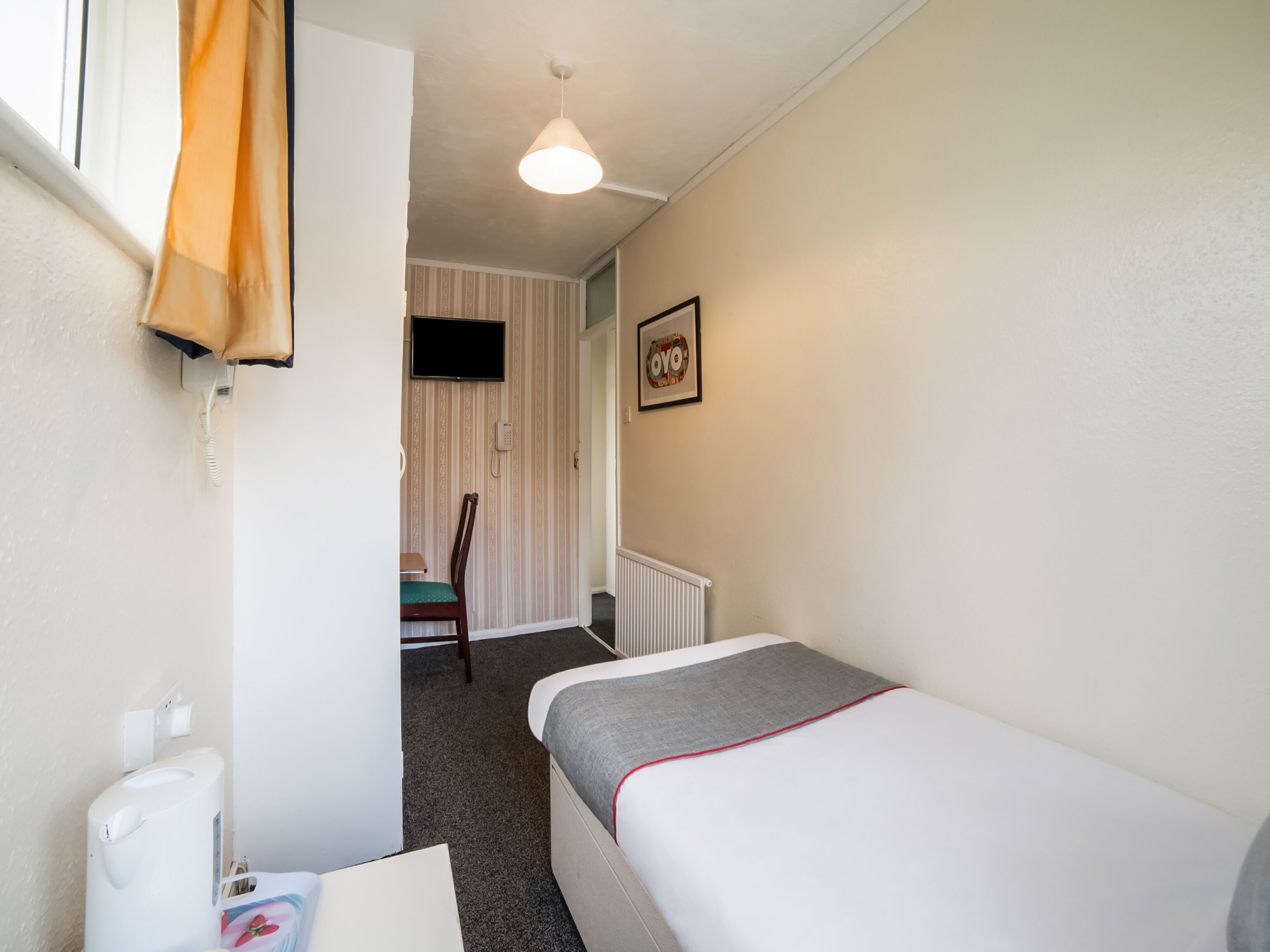 A small, clean room with a single bed, a chair, a toilet, and a TV.