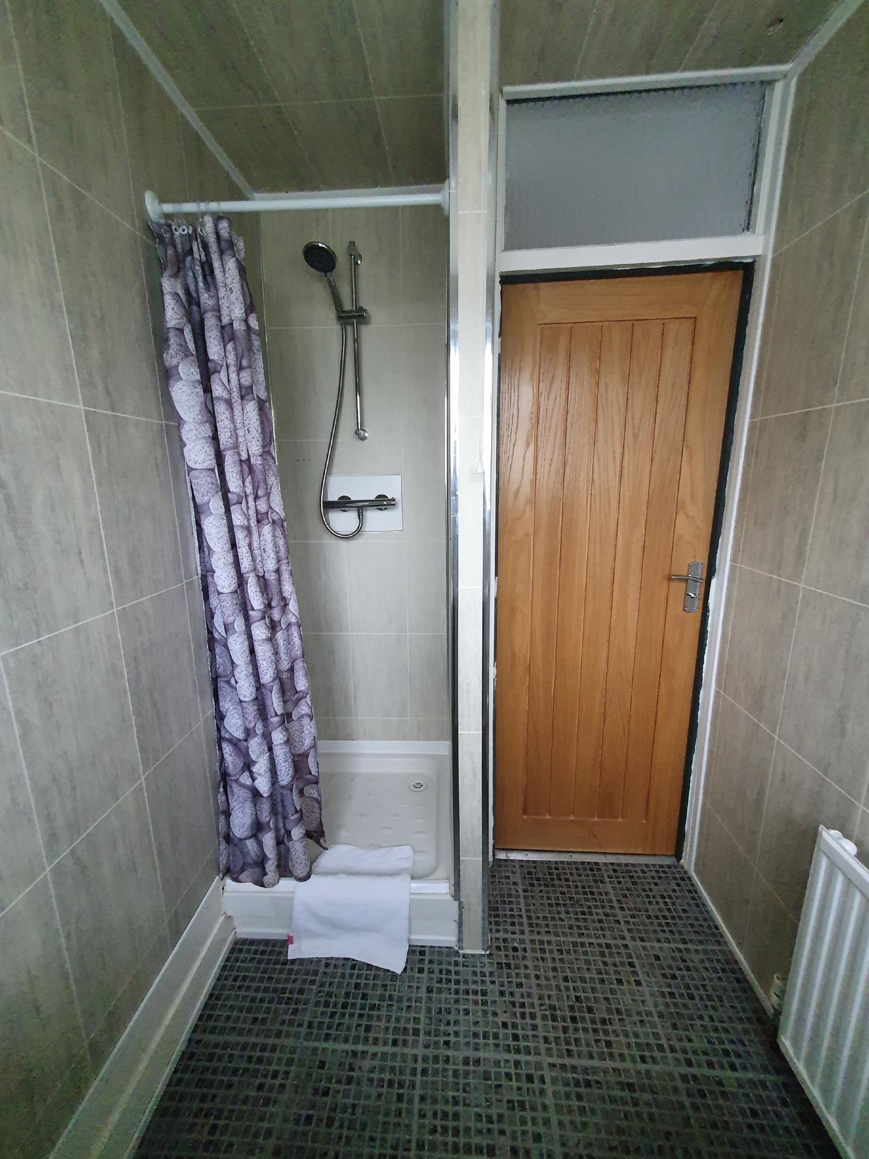 A bathroom with a shower, a wooden door, and a tiled floor.