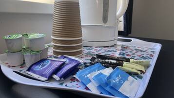 A tray with coffee pods, a stack of paper cups, and a white coffee maker on a floral tablecloth.