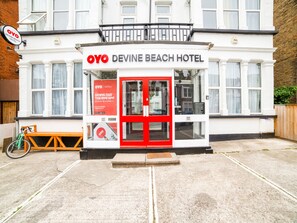 La façade de l’hôtel Devine Beach, avec sa porte rouge bien visible et une enseigne faisant la publicité de l’application OYO.