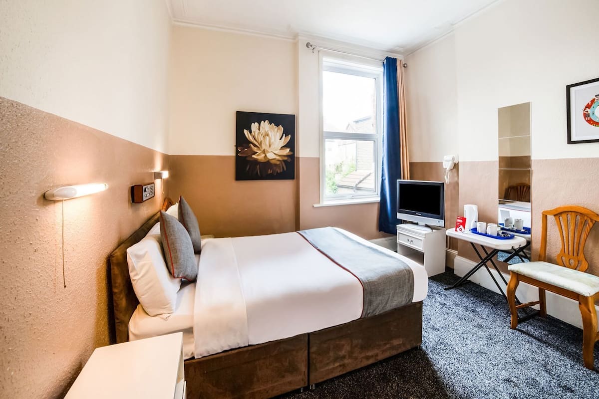 Une chambre d’hôtel comprenant un lit, une table de chevet, une télévision, un bureau, une chaise et des œuvres d’art.
