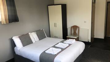 A neatly made bed with white and grey bedding, a wooden chair, a wardrobe, and a radiator.