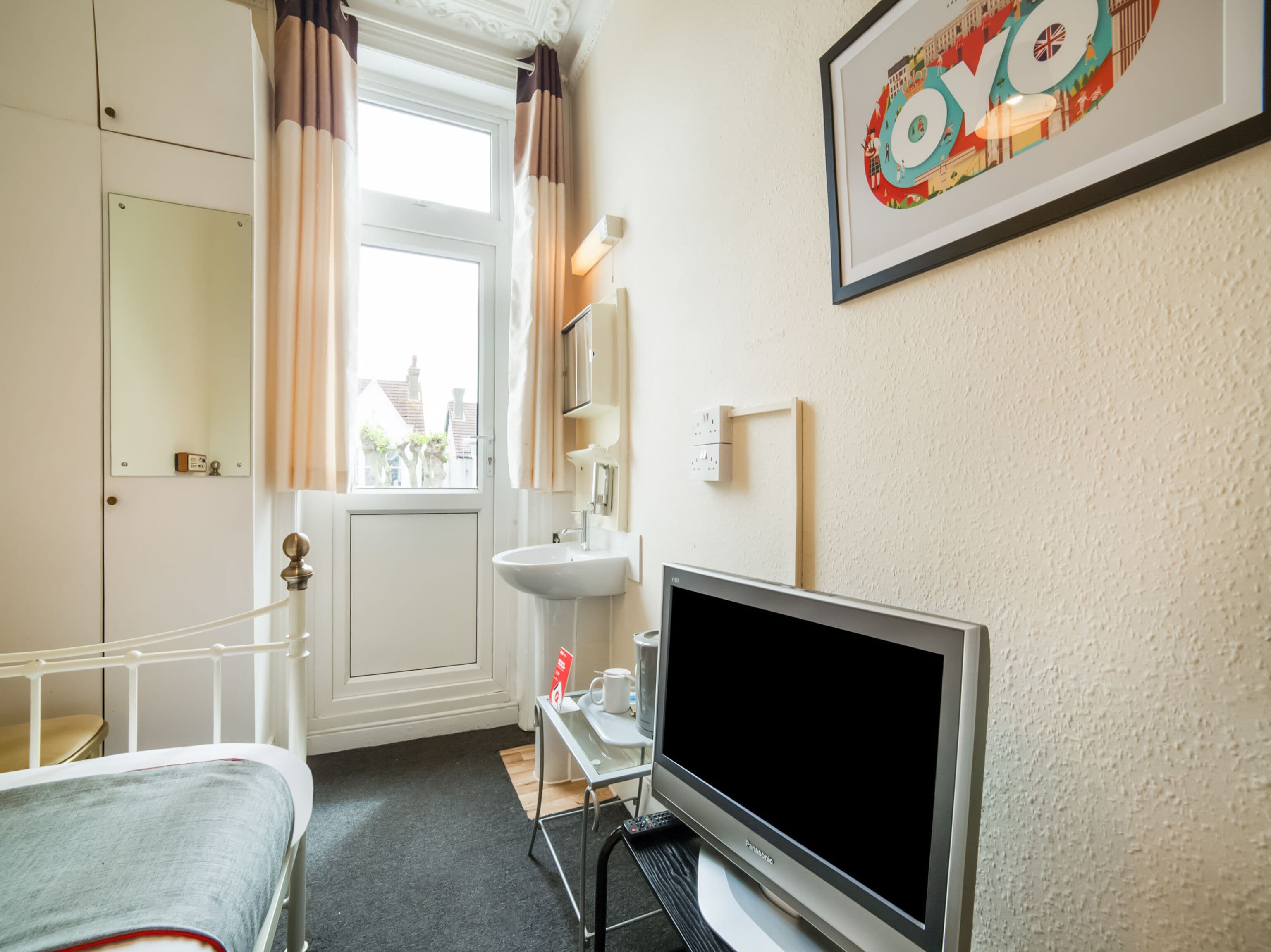 Hotelkamer met een bed, televisie, nachtkastje, raam met gordijnen, spiegel en een ingelijste foto aan de muur.