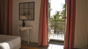 A hotel room with a bed, a small table with a lamp, a framed picture, and a balcony with red and white striped curtains. - Marina Hotel Charming Rooms (Finale Ligure)