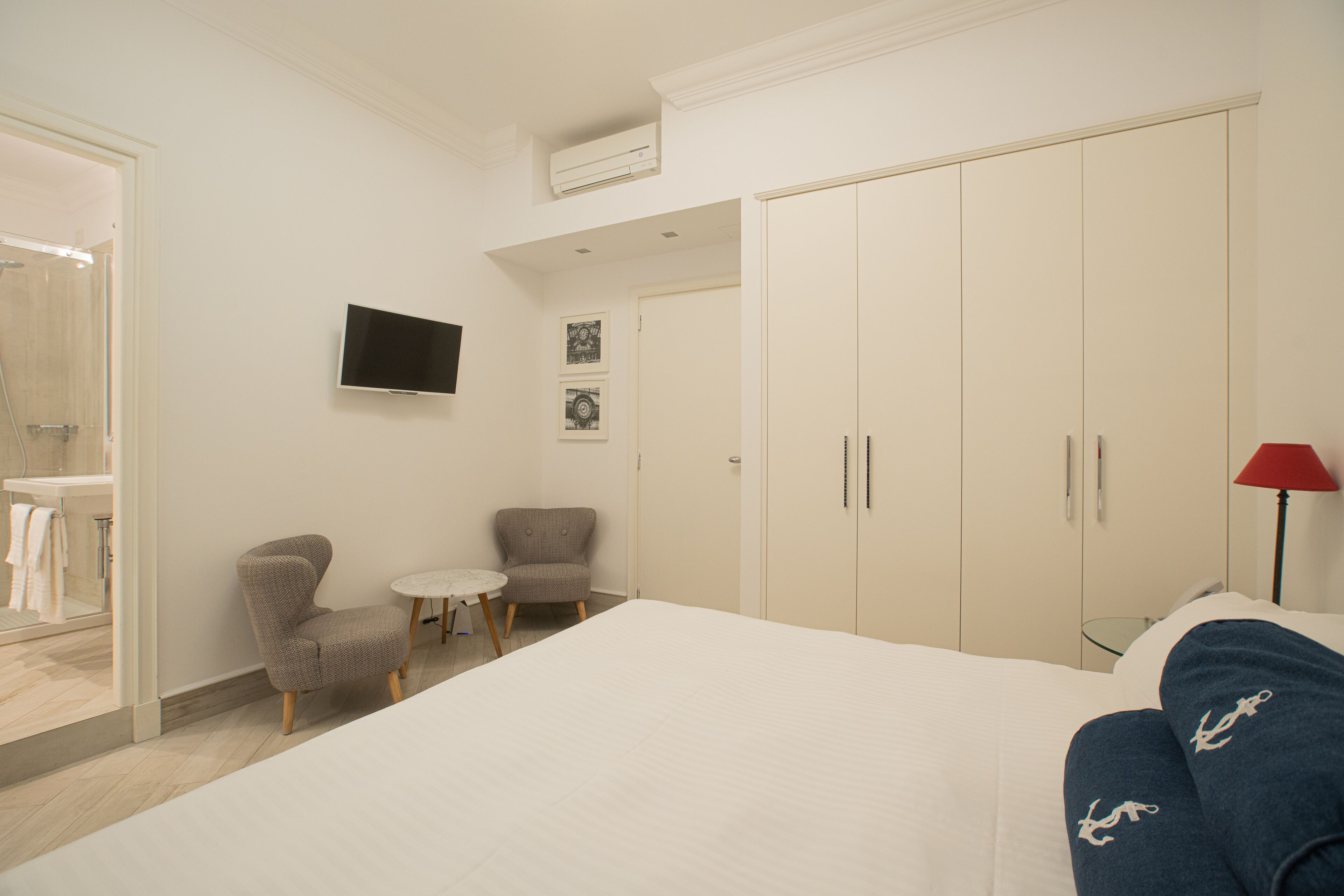 Une chambre d’hôtel comprenant un lit, un téléviseur fixé au mur, une armoire, une chaise et une petite table.