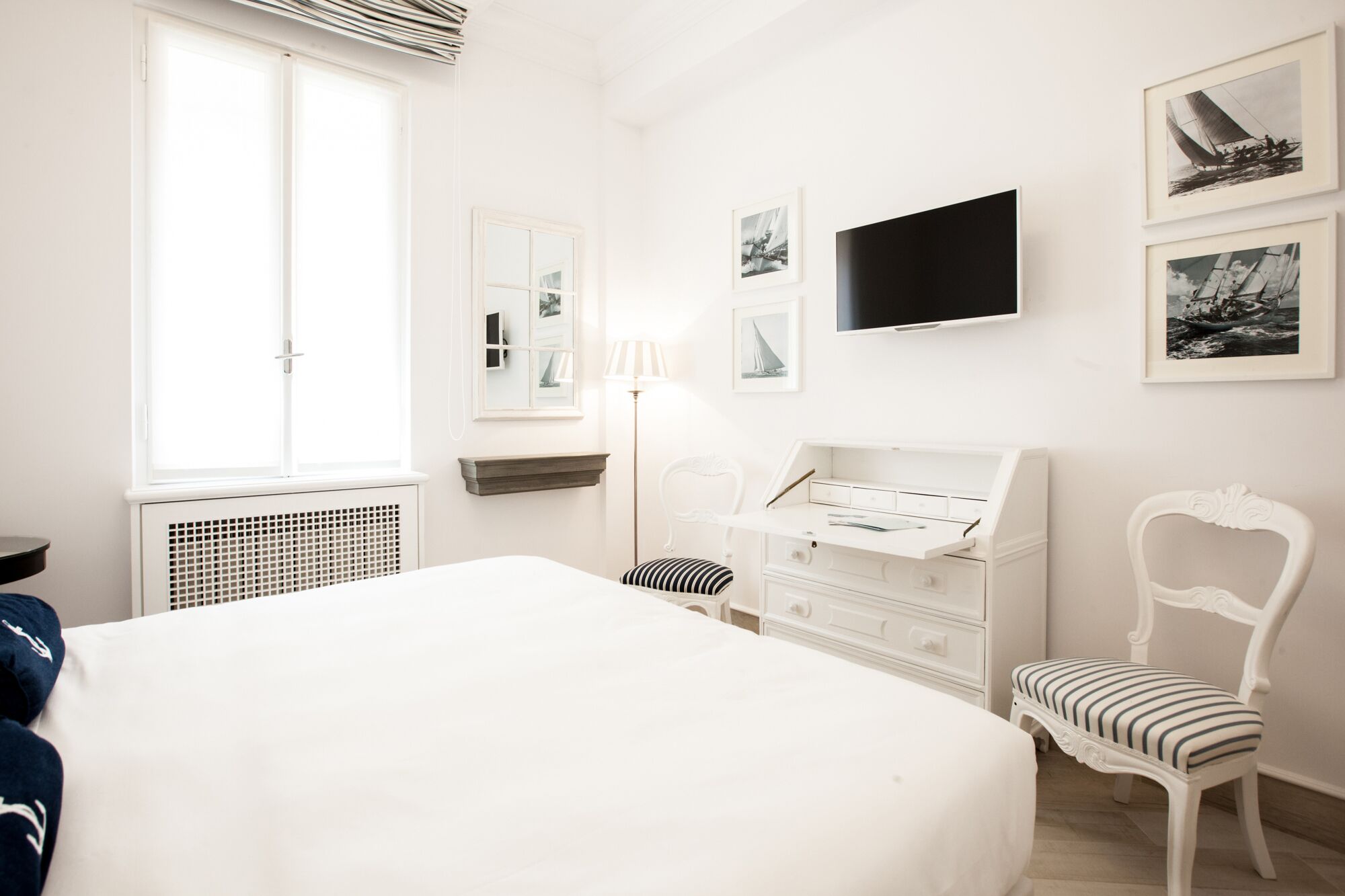 A bedroom with a large bed, a desk, a chair, a TV, and framed pictures on the wall.