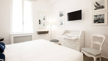 Un dormitorio con una cama grande, un escritorio, una silla, un televisor y cuadros en la pared.