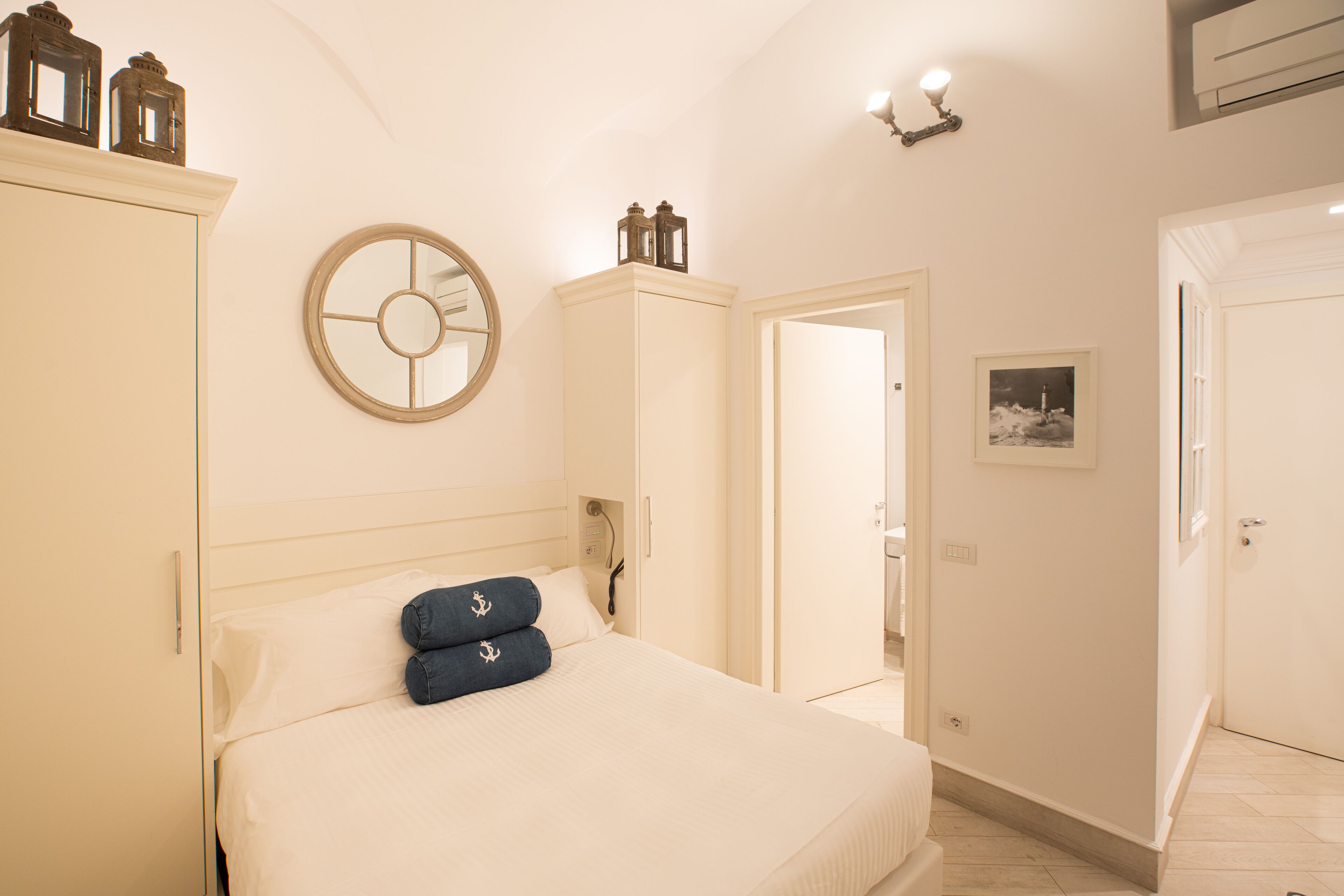 A bedroom with a bed, a wardrobe, a mirror, and a door leading to another room.