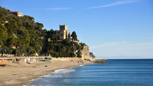 A coastal scene with a castle on a hill, a beach, and a clear sky. - Marina Hotel Charming Rooms (Finale Ligure)
