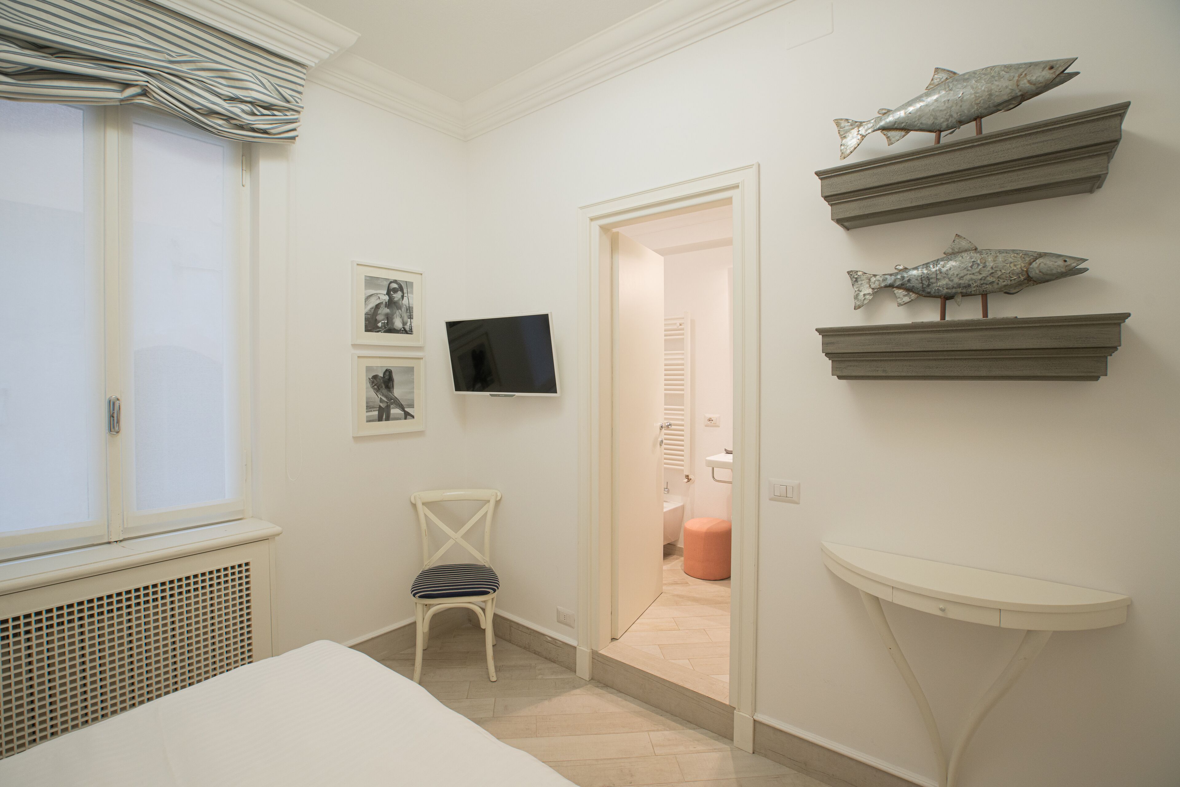 A bedroom with a bed, a chair, a TV, and wall-mounted shelves with fish decorations.