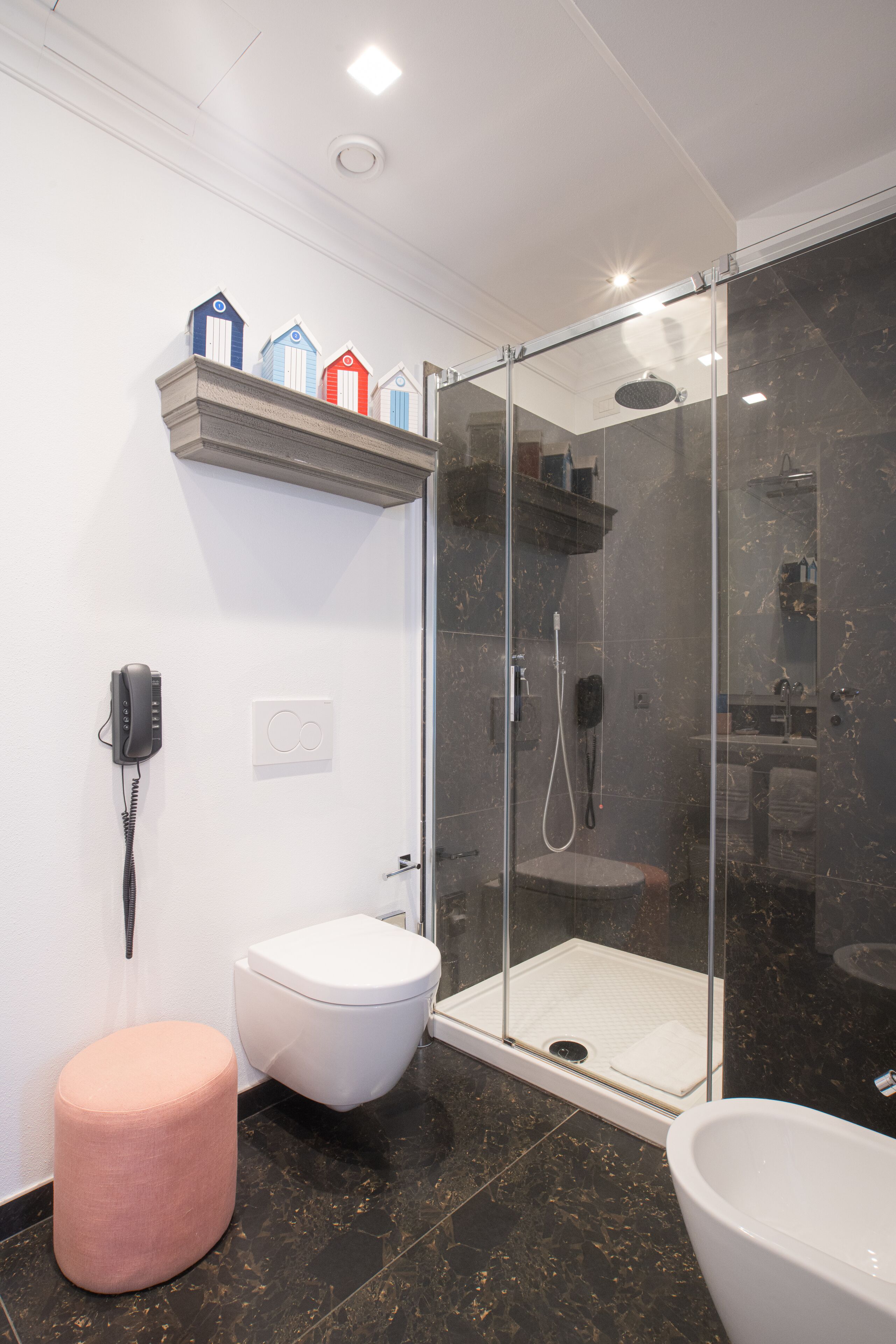 A modern bathroom with a glass-enclosed shower, a white toilet, a pink ottoman, and a white bathtub.