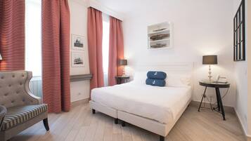 Une chambre d’hôtel avec un grand lit, une chaise, une table de chevet avec une lampe et une étagère murale agrémentée d’objets décoratifs.