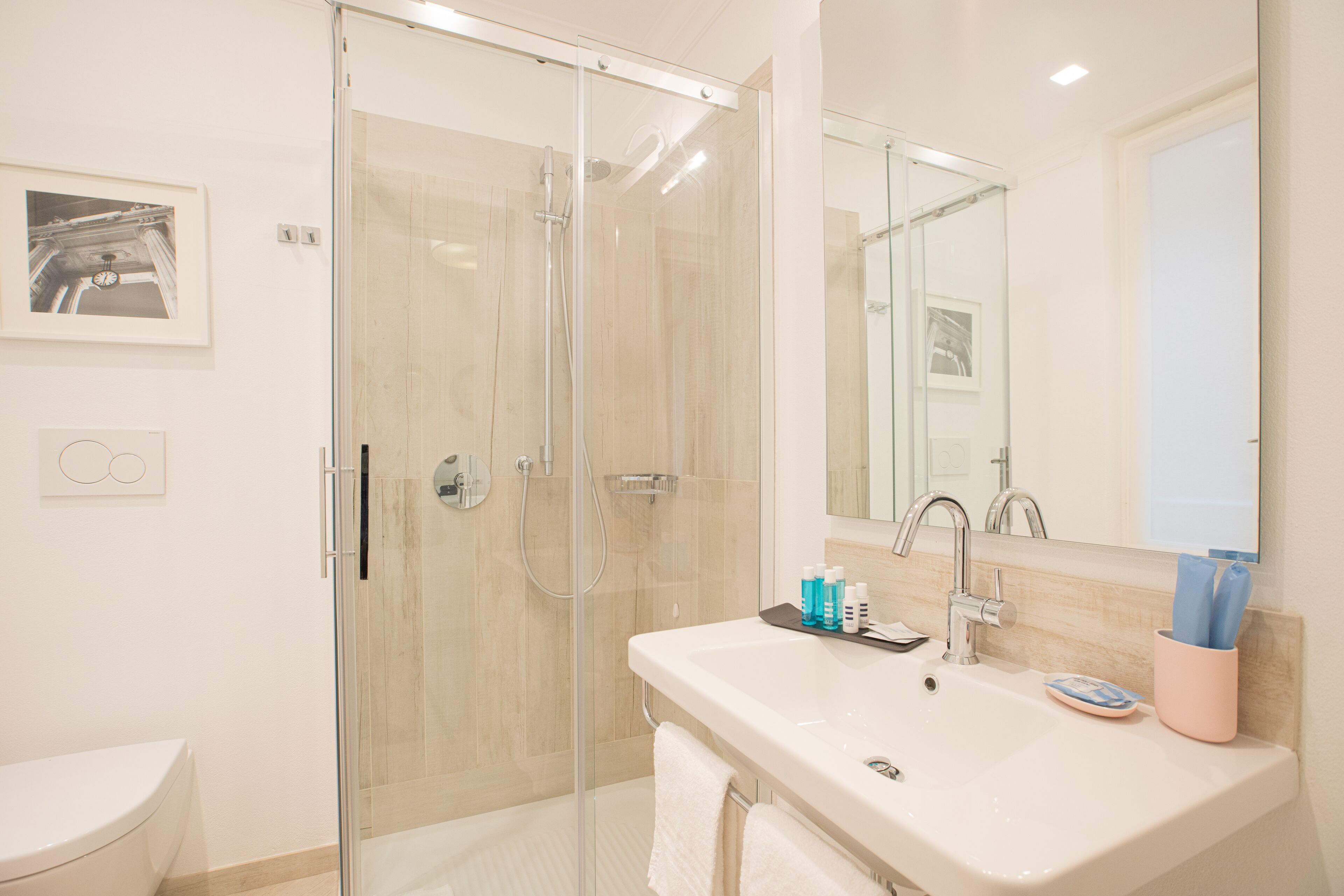 A modern bathroom with a glass-enclosed shower, a white sink with toiletries, and a large mirror.