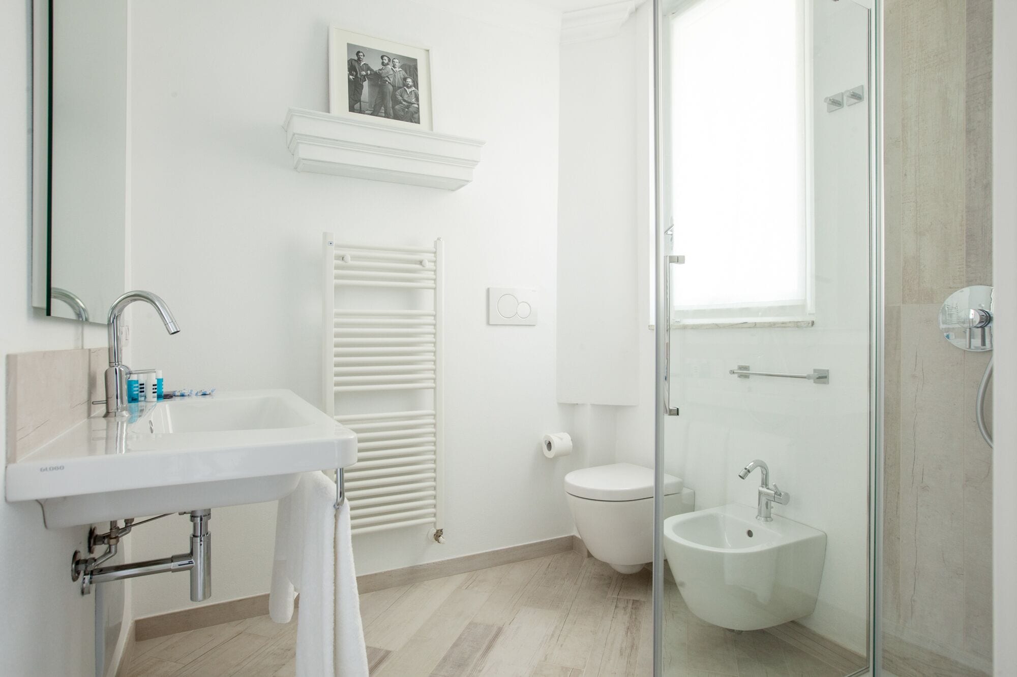 A modern bathroom with a white sink, a glass shower enclosure, a toilet, and a bidet.
