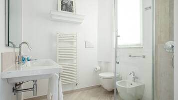 Un baño moderno con un lavabo blanco, cabina de ducha con mampara de vidrio, inodoro y bidé.