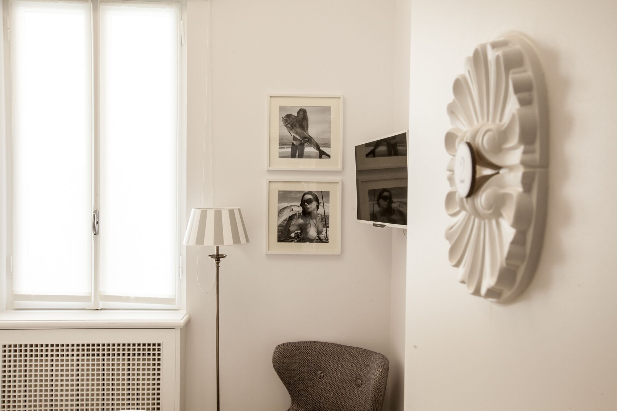 Una habitación con un ventanal grande, un radiador, una lámpara y cuadros en la pared.