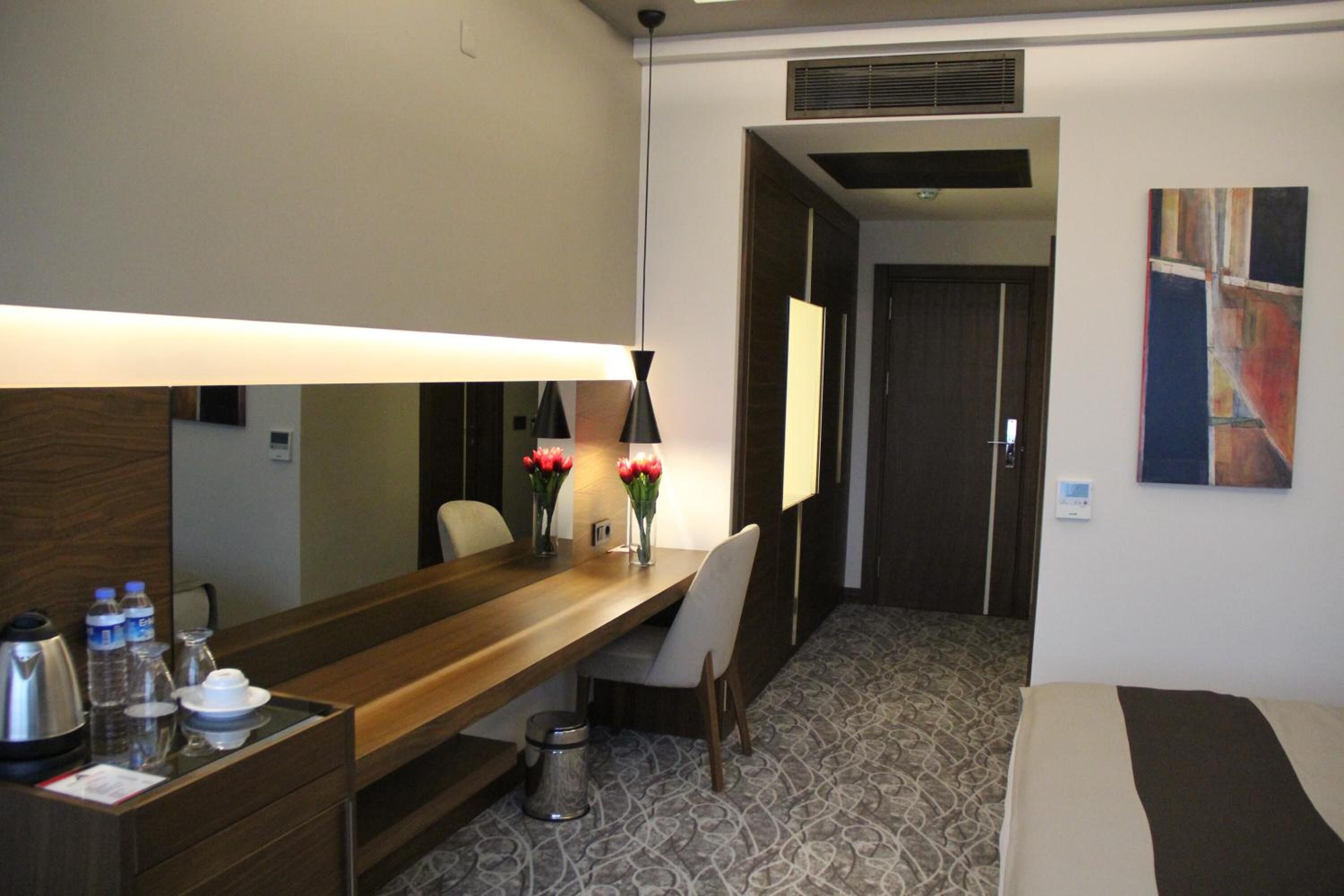 A hotel room with a wooden desk, a chair, a bed, a lamp, and a painting on the wall.