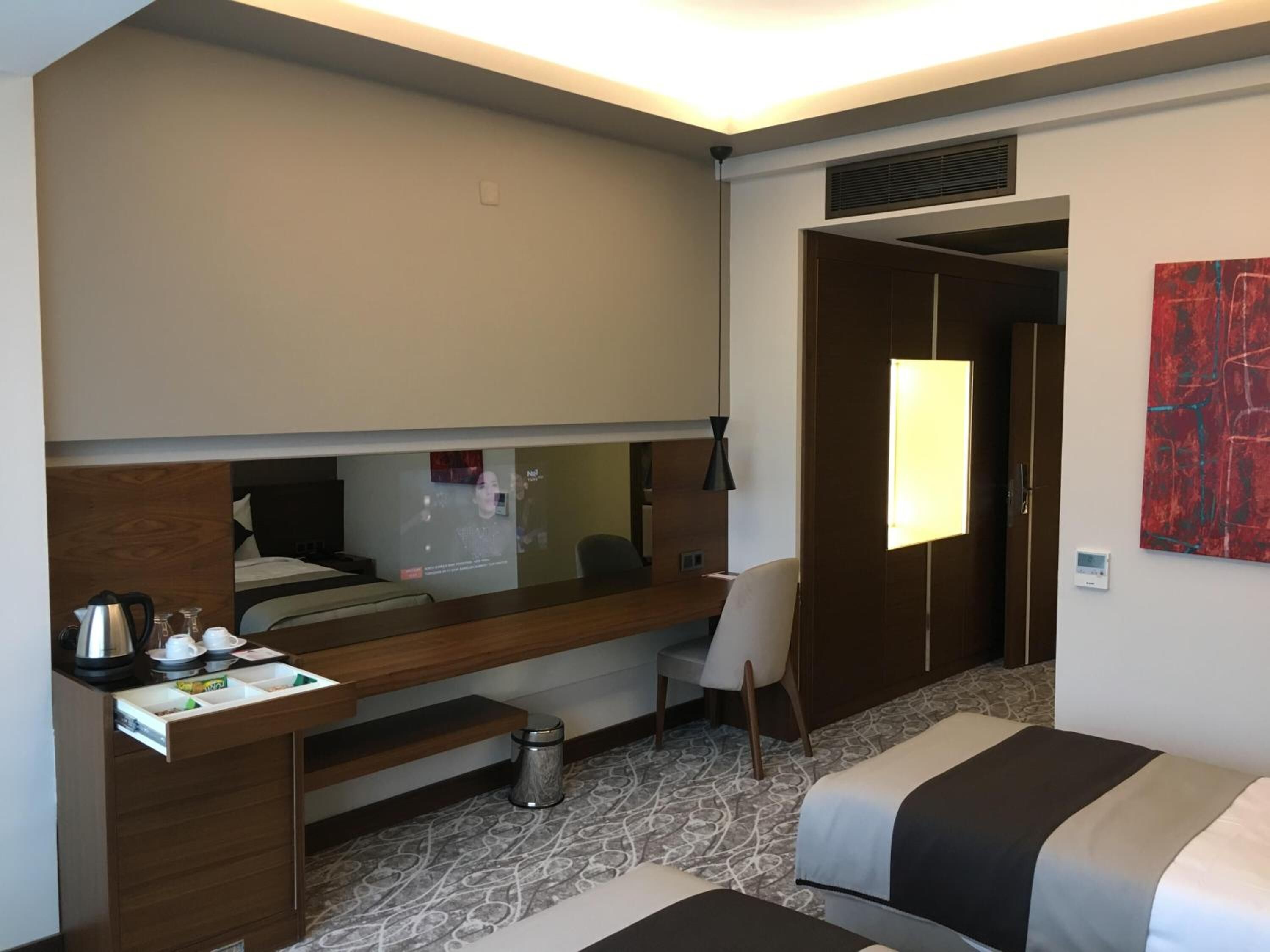 Une chambre d’hôtel comprenant un lit, un bureau, une chaise, une petite poubelle et un grand miroir.