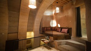 A rustic interior with a wooden staircase, a cushioned seating area, and pendant lighting. - Helike Cave Suites (Nevsehir)
