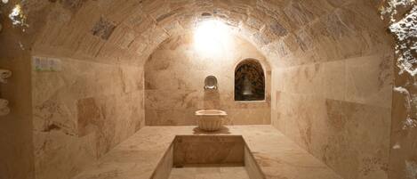 A stone-walled room with a central basin, an arched niche, and a small window.