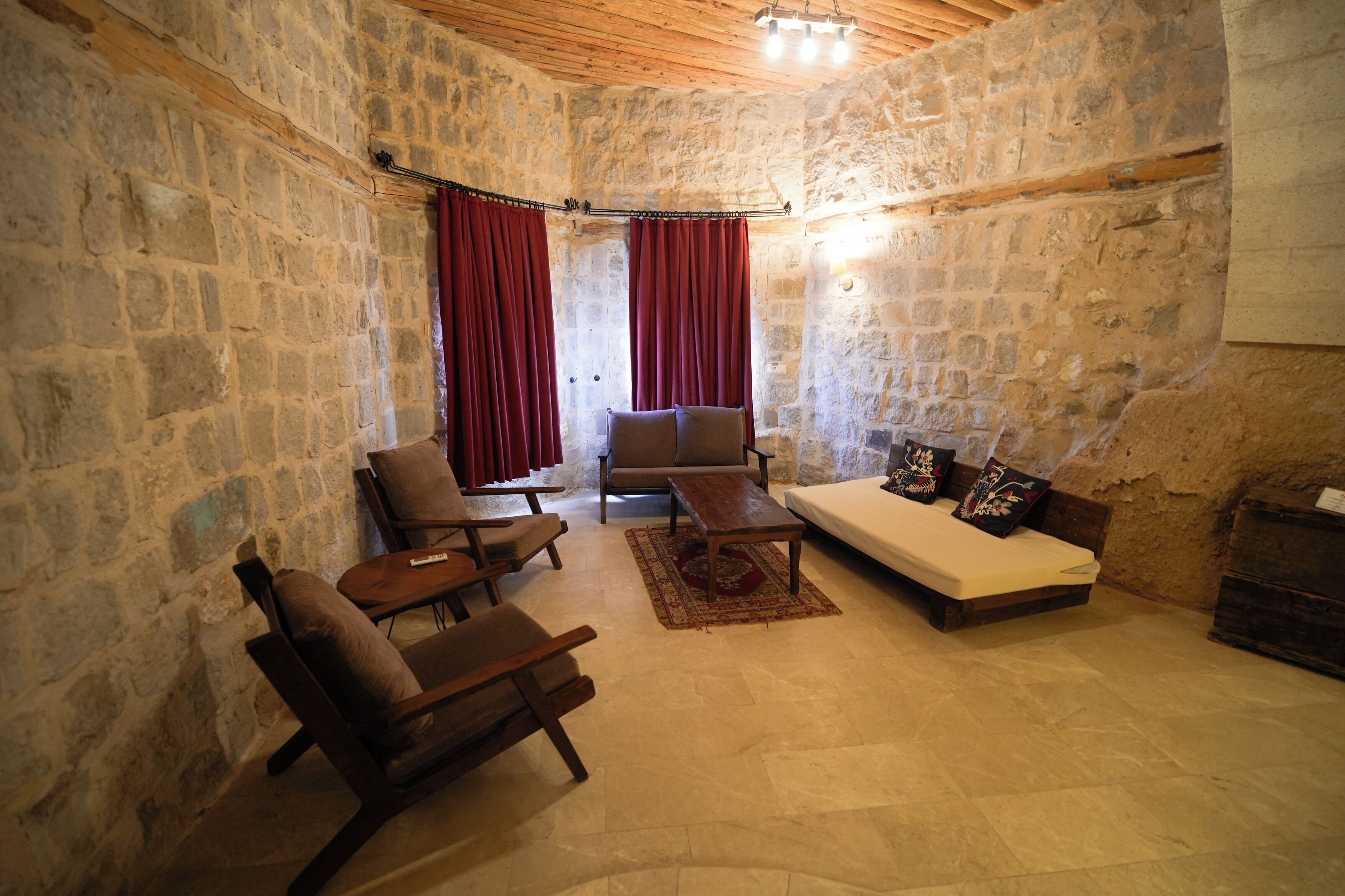 A stone-walled room with a sofa, two armchairs, a coffee table, and a wooden ceiling.