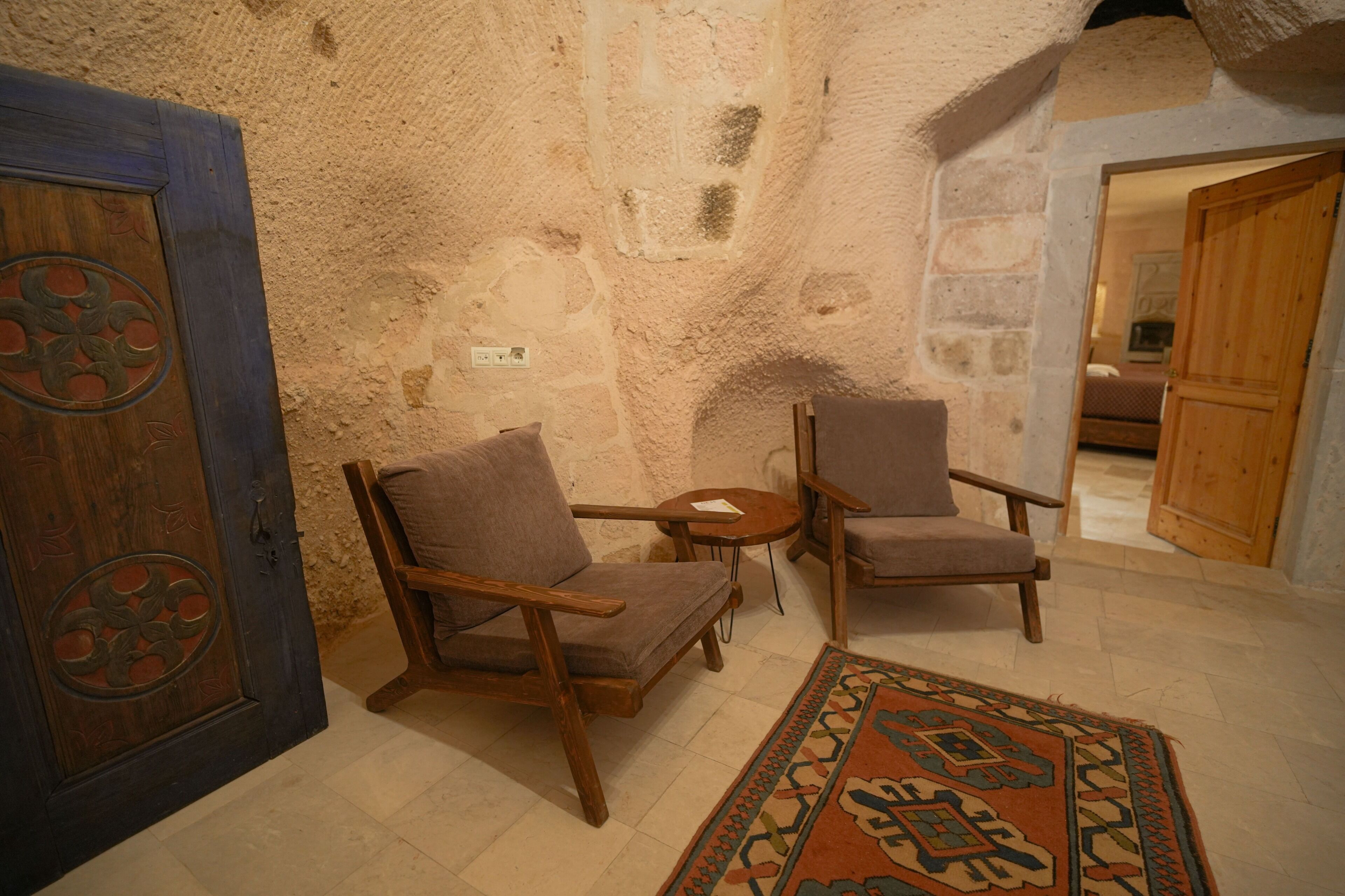 Une pièce avec un mur en pierre, deux chaises en bois, une petite table ronde et un tapis à motifs.