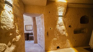 A stone-walled interior with a doorway leading to another room, a light fixture on the wall, and a tiled floor. - Helike Cave Suites (Nevsehir)