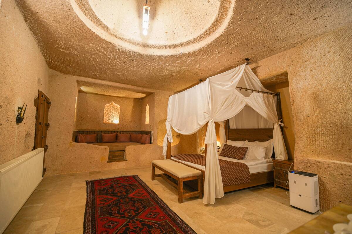 A room with a four-poster bed, a bench, a red patterned rug, and a small window.