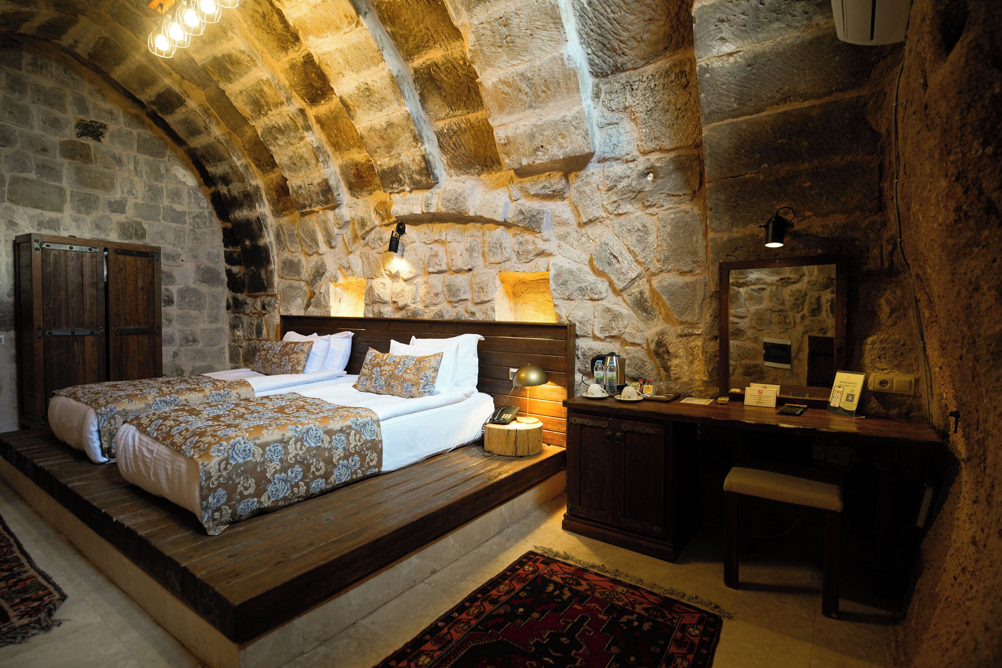 Un dormitorio con paredes de piedra, una cama, una mesita de noche y un escritorio con una silla.