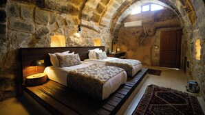 A stone-walled bedroom with two beds, a wooden bench, a rug, and a skylight. - Helike Cave Suites (Nevsehir)
