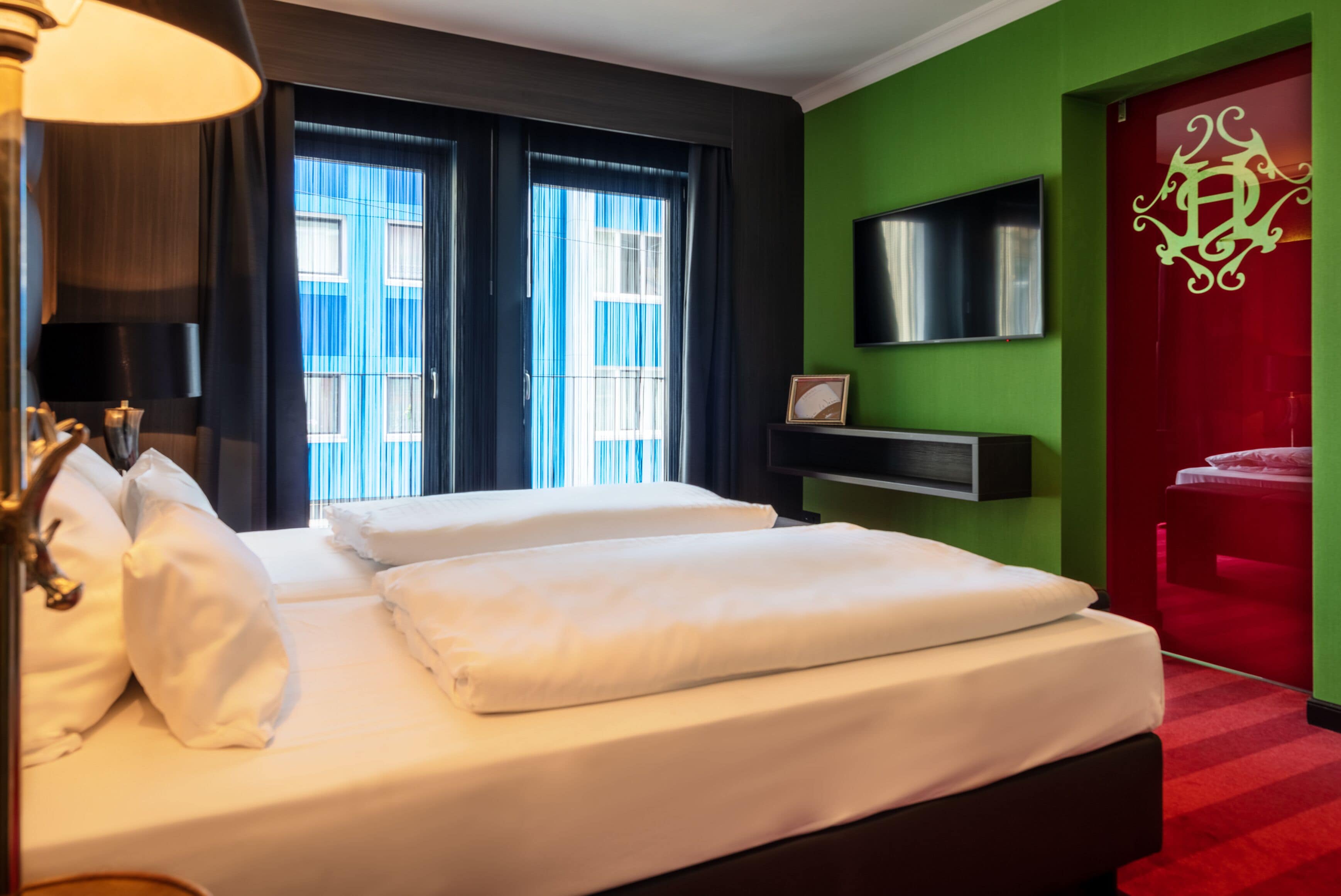 A hotel room with a bed, a TV, and a red door.