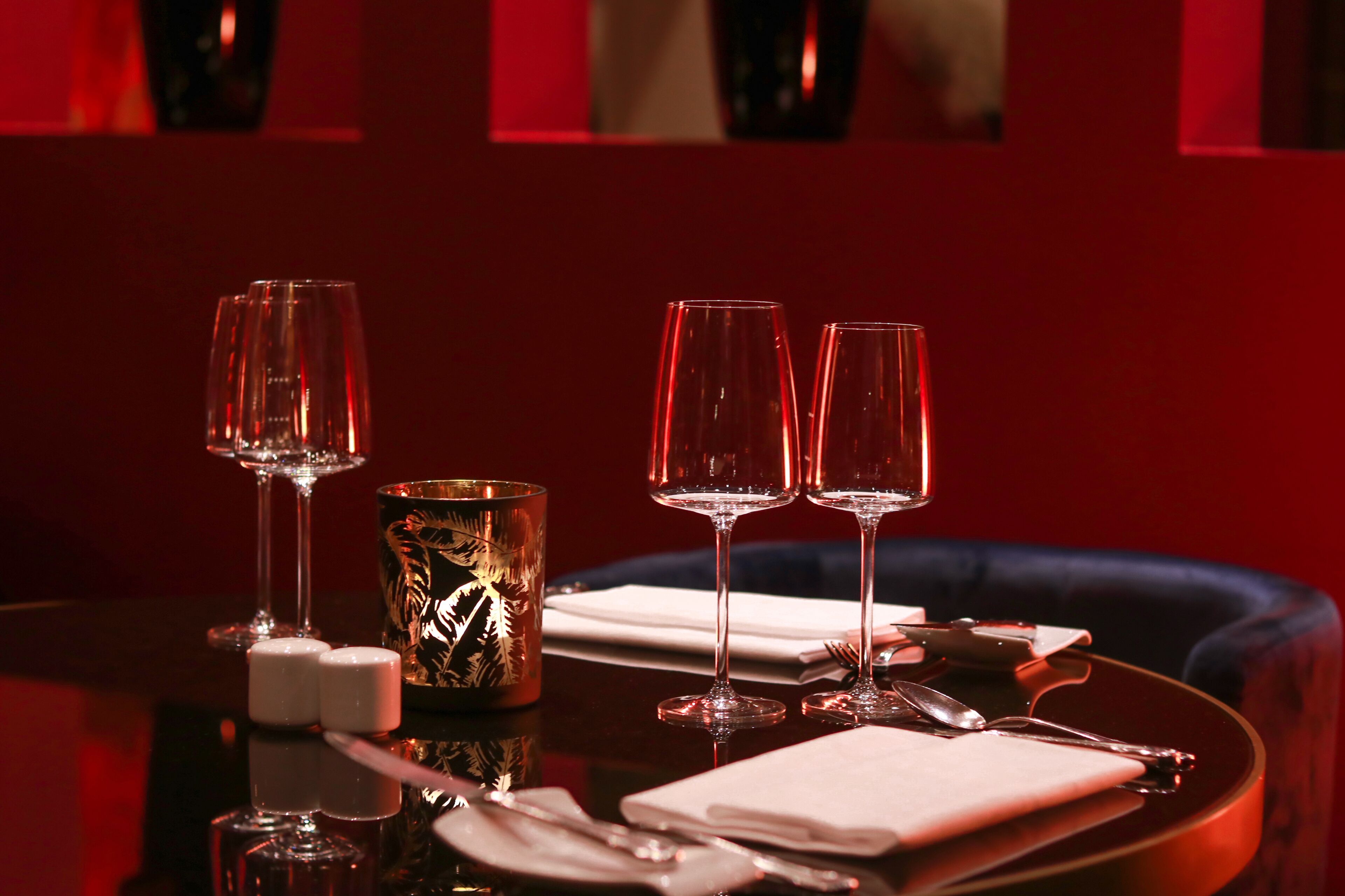 A dining table set with two wine glasses, a candle, salt and pepper shakers, a napkin, and cutlery.