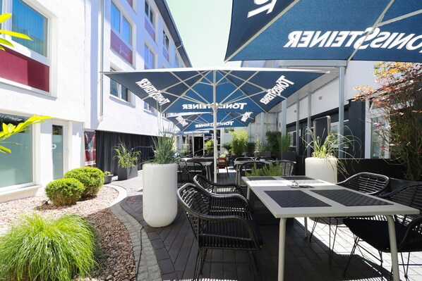 An outdoor seating area with tables and chairs, umbrellas, and potted plants. - Haverkamp Suites (Bremerhaven)