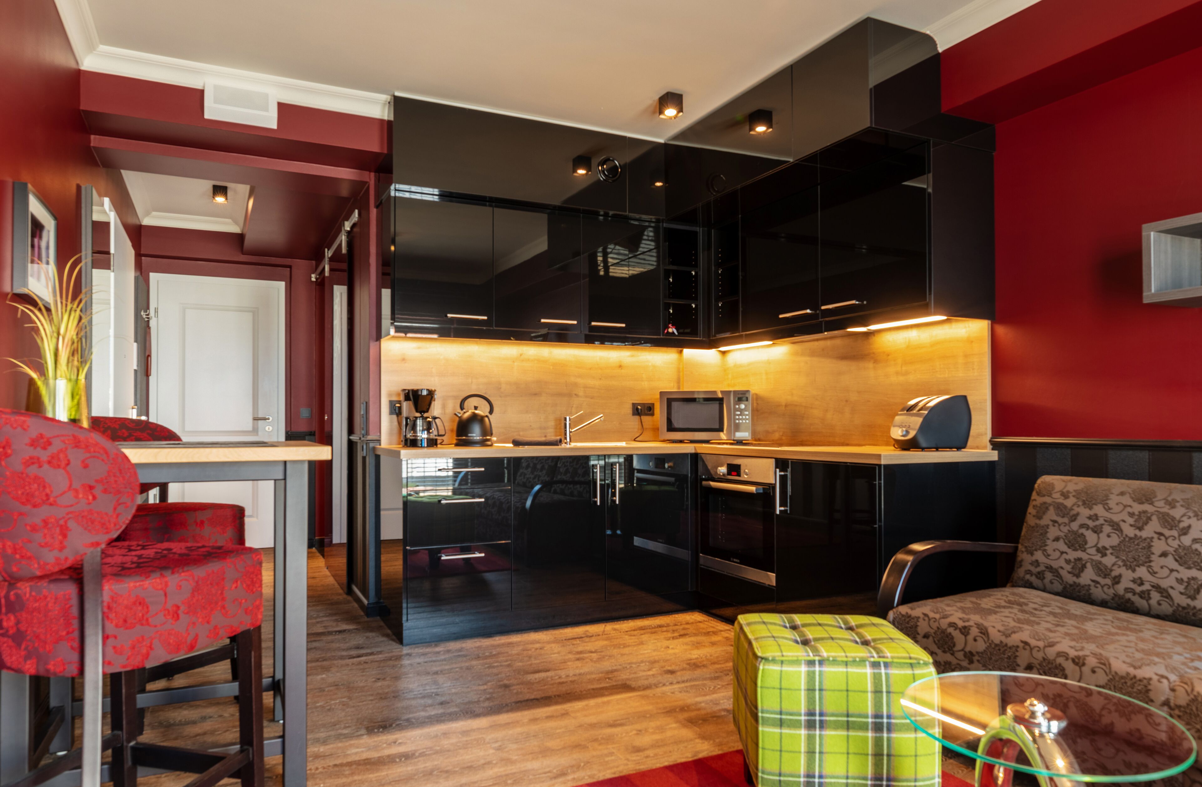 A compact living space with a kitchenette, a dining area with red upholstered chairs, and a sofa with a patterned cushion.