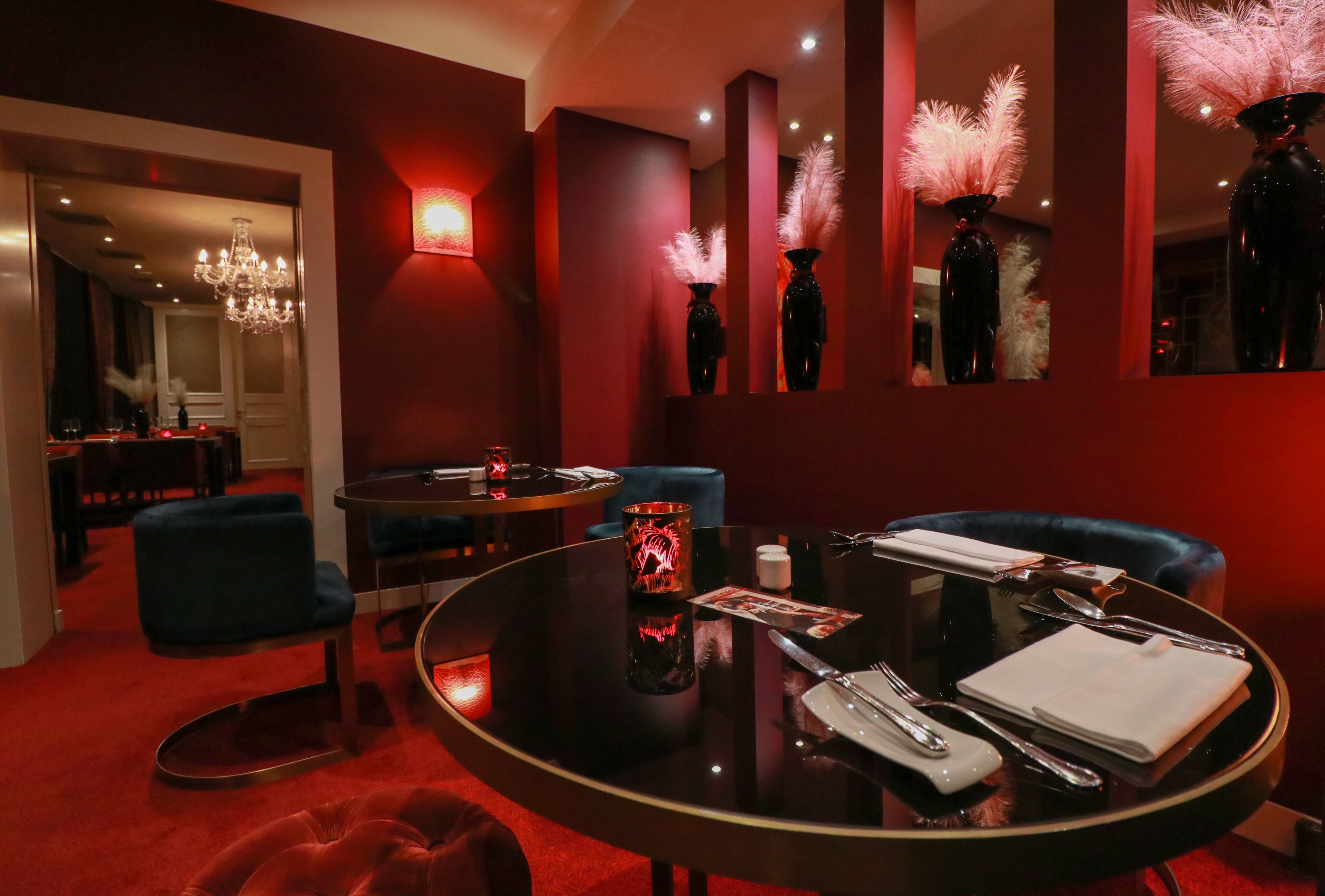 A dimly lit room with a round table set for dining, a blue chair, and a red carpet.