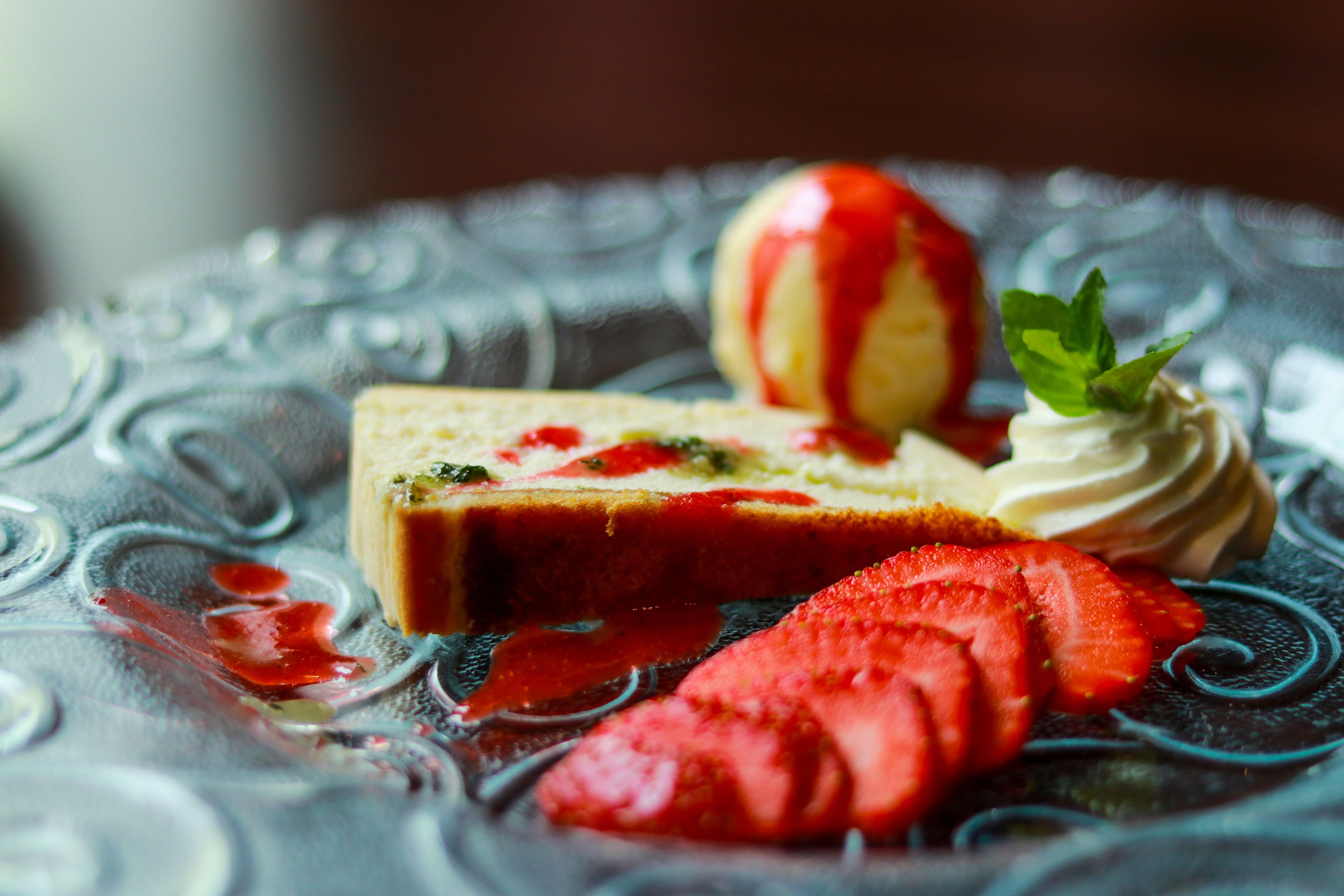 Un postre con una porción de pastel, fresas y una bola de helado sobre un plato estampado.