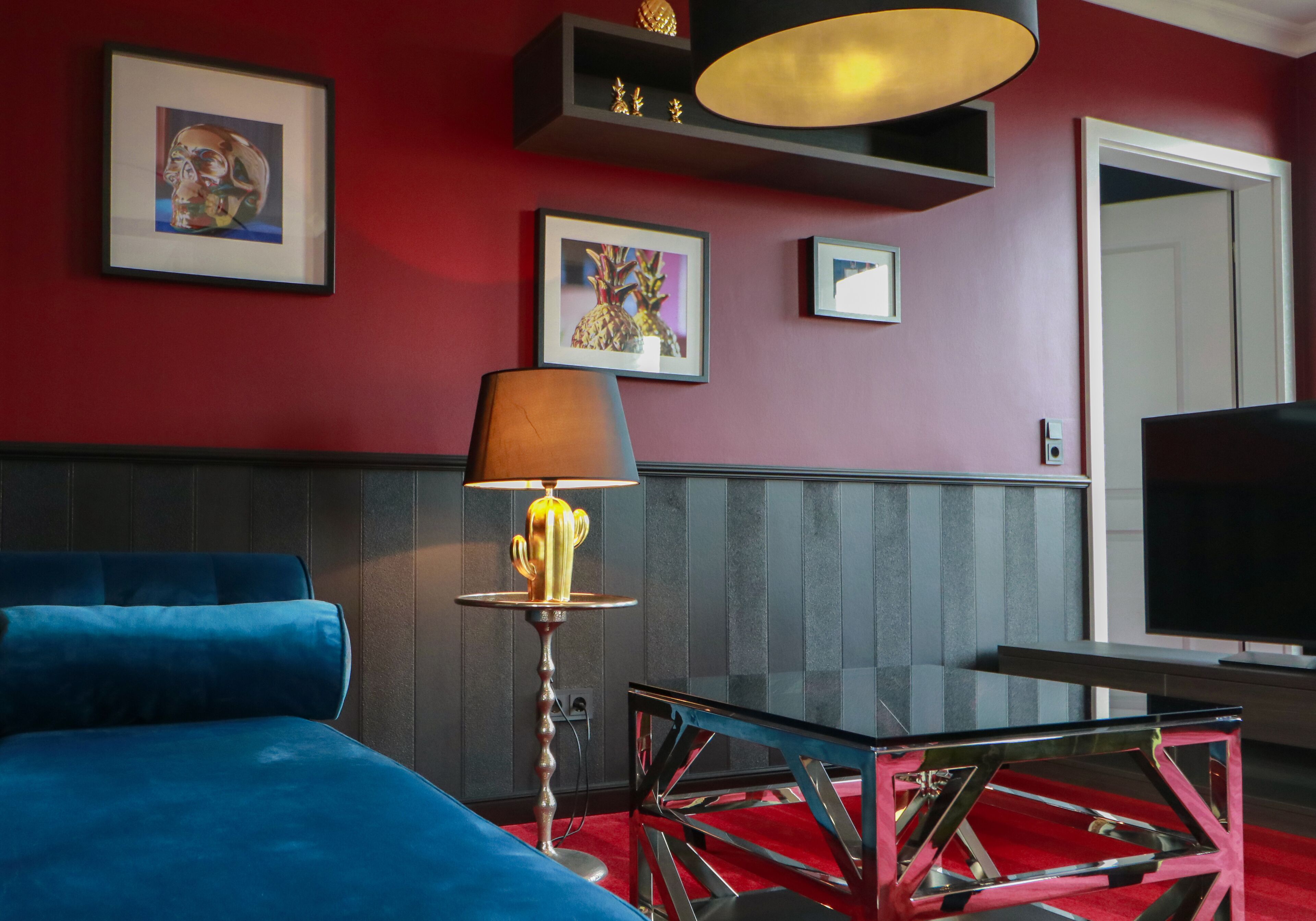 A room with a blue sofa, a glass coffee table, a lamp, framed artwork on the wall, and a television.