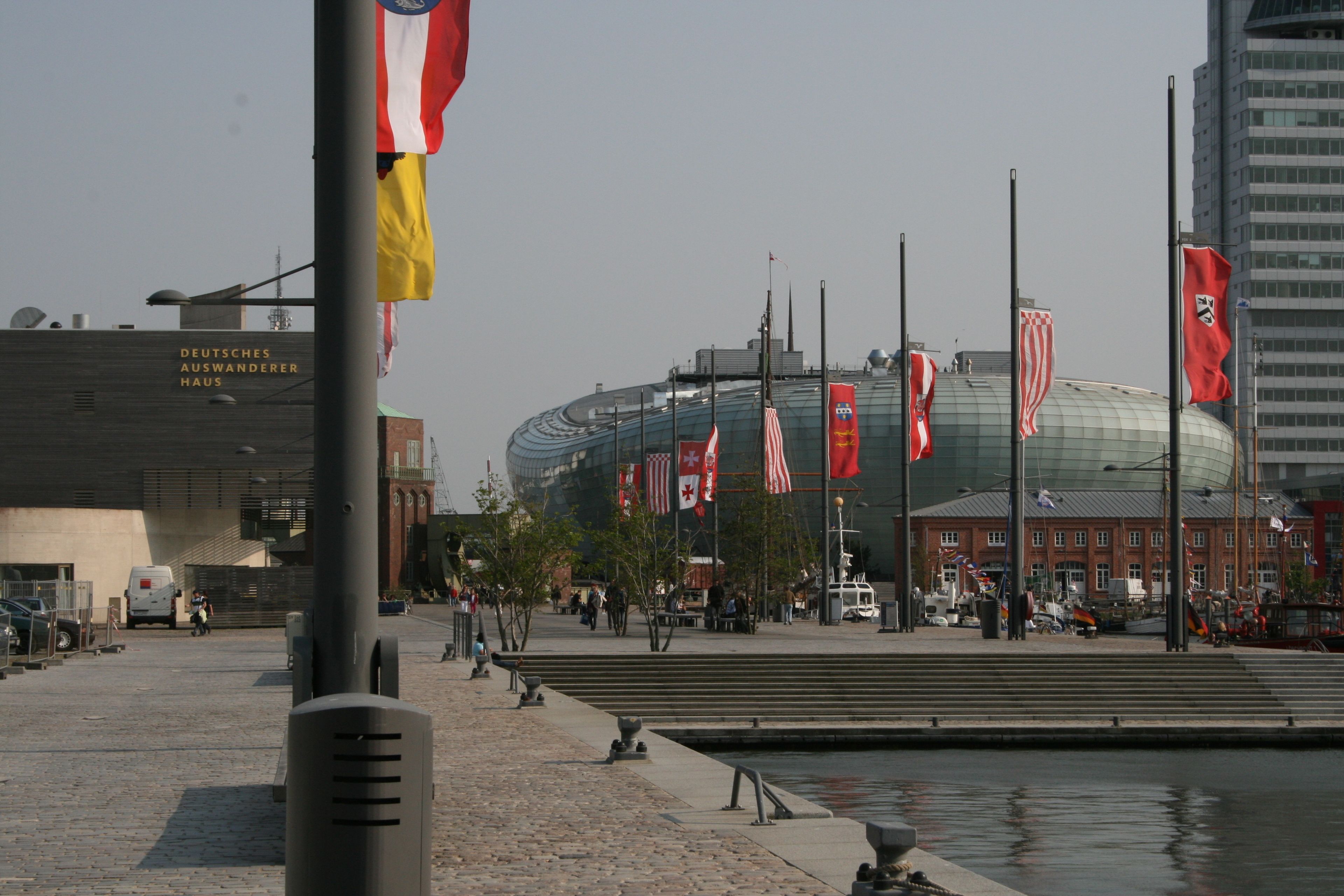 A stadium with multiple flags, a water body, and a building labeled "DEUTSCHES AUSWANDERER HAUS".