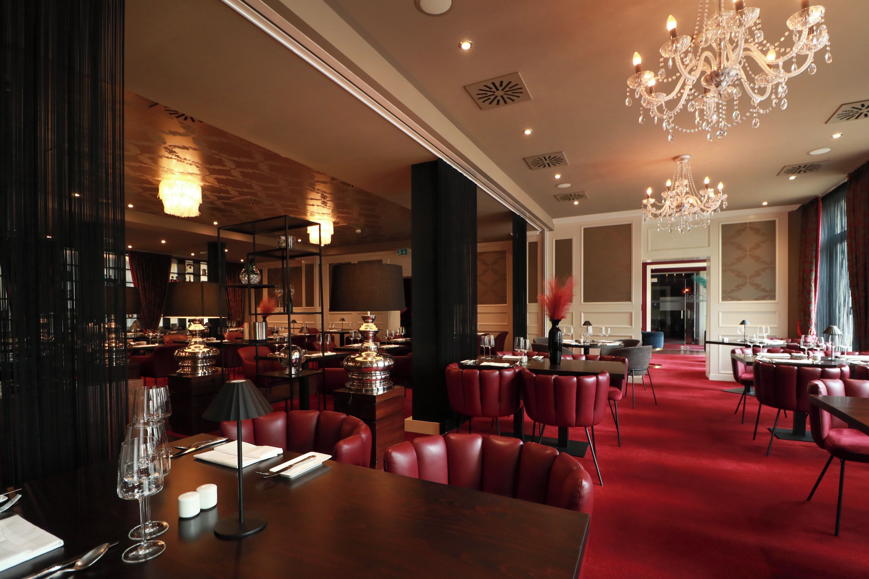 A spacious hotel lobby with red leather seating, chandeliers, and a bar area.