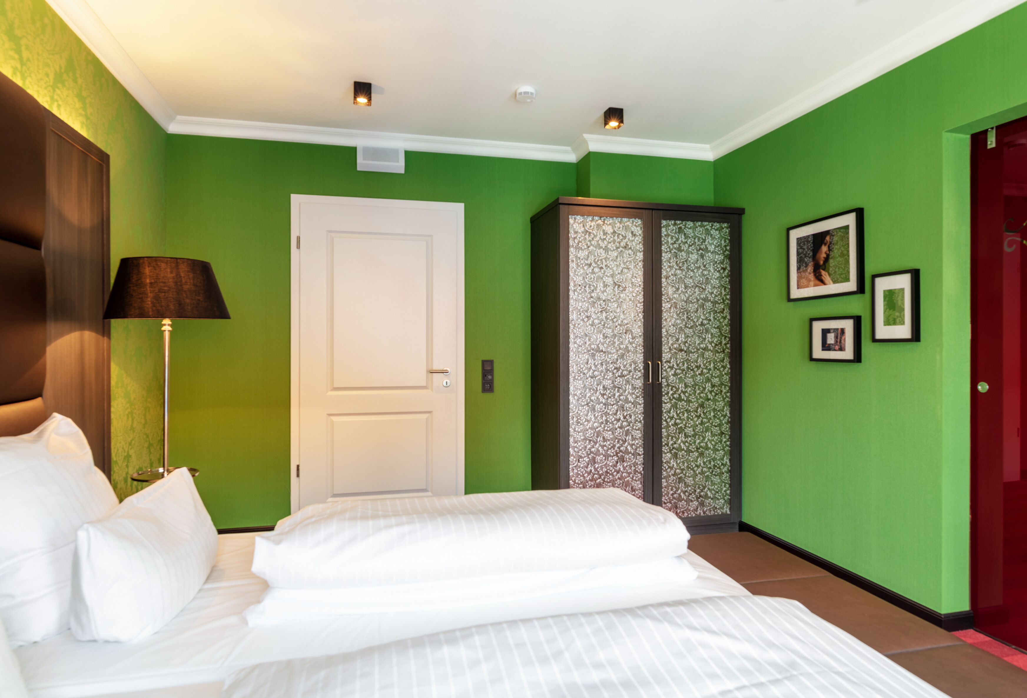 Une chambre d’hôtel avec un lit, une armoire, une lampe et une porte.