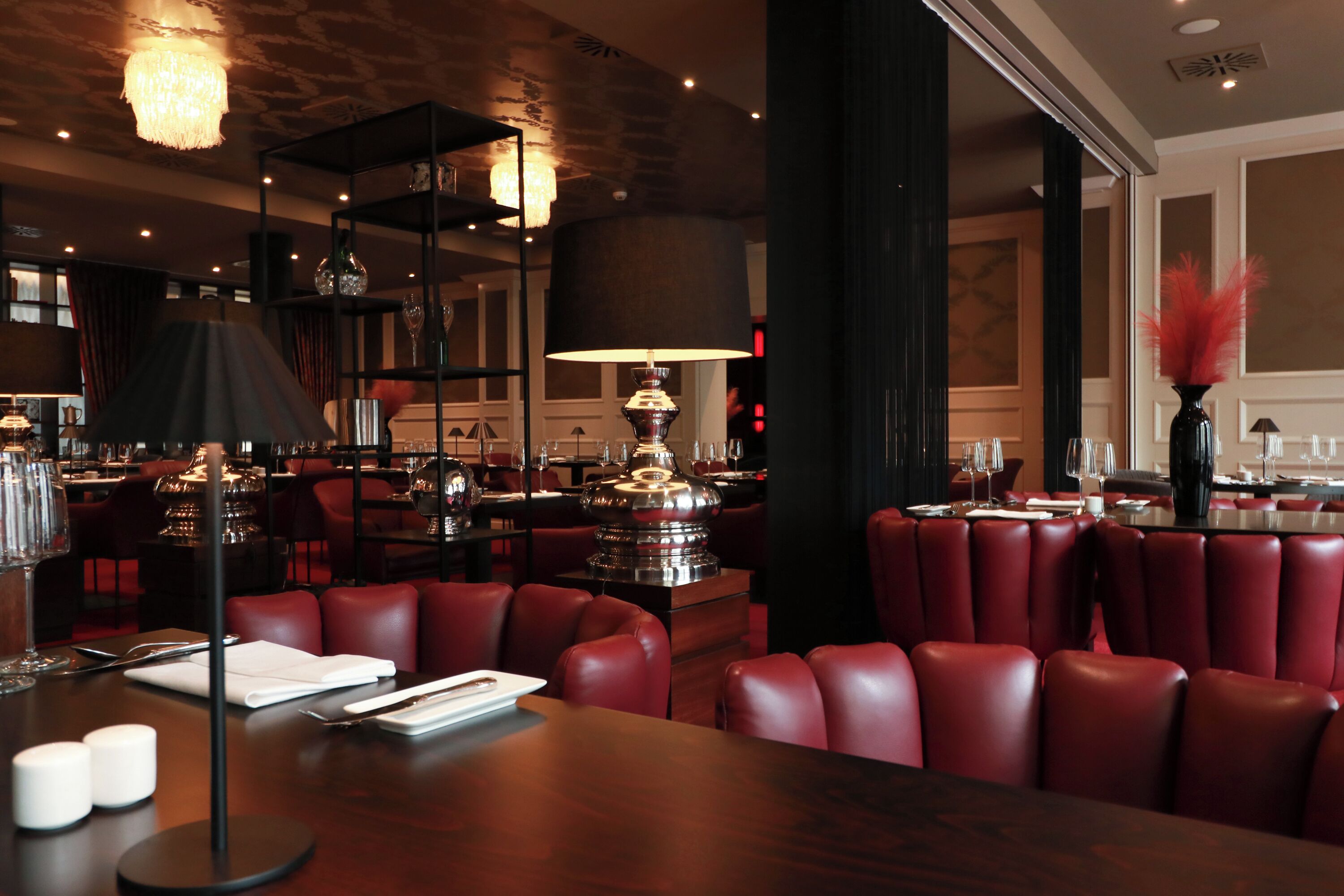 Un restaurante con asientos de cuero rojo, un candelabro y una mesa grande con una lámpara.