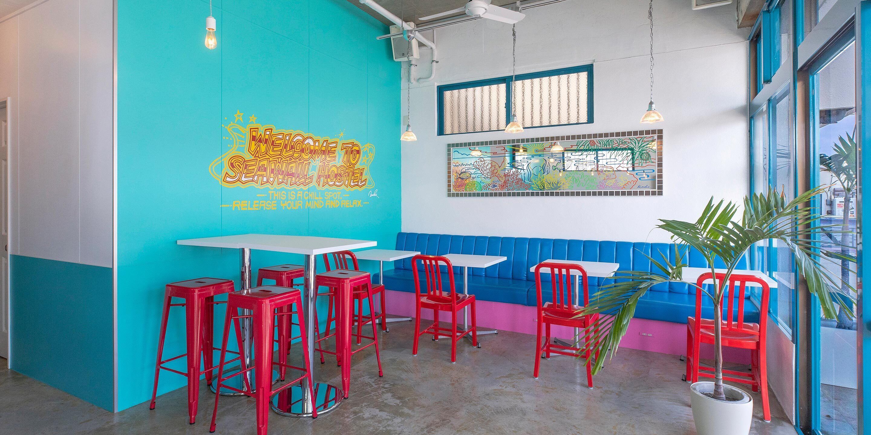 A vibrant hostel interior with teal walls, red chairs, and a mural welcoming guests.