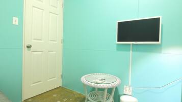 A room with teal walls, a white door, a small round table with a glass top, and a mounted flat-screen TV.
